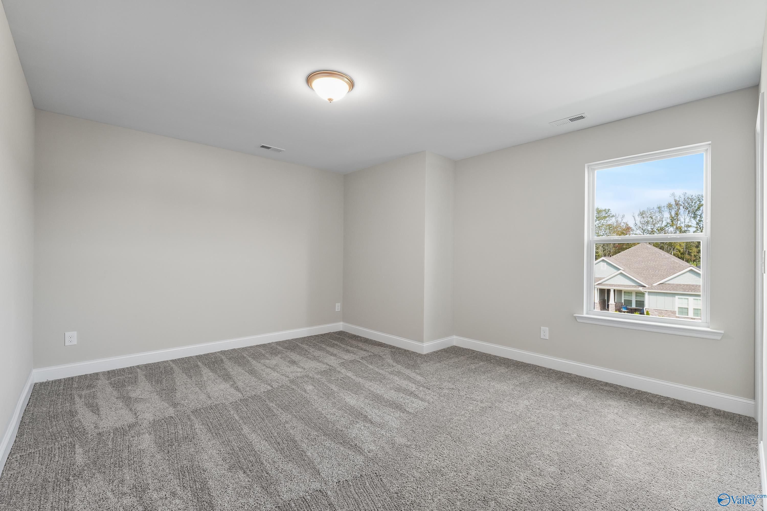 Spacious empty bedroom with gray walls, carpet, and window overlooking neighborhood in Evermore Homes The Haven, Owens Cross Roads, Alabama