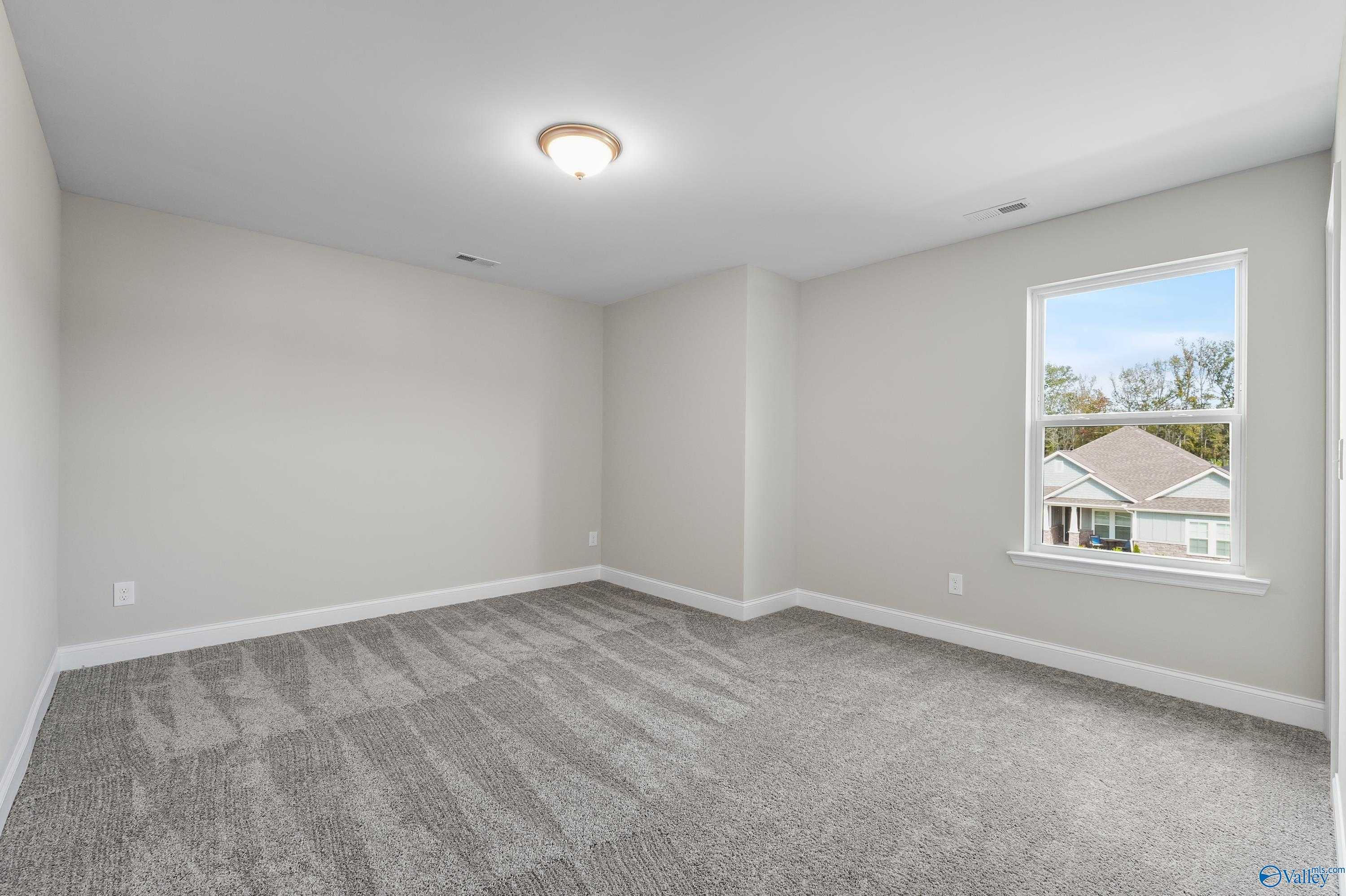Spacious empty bedroom with gray walls, carpet, and window overlooking neighborhood in Evermore Homes The Haven, Owens Cross Roads, Alabama