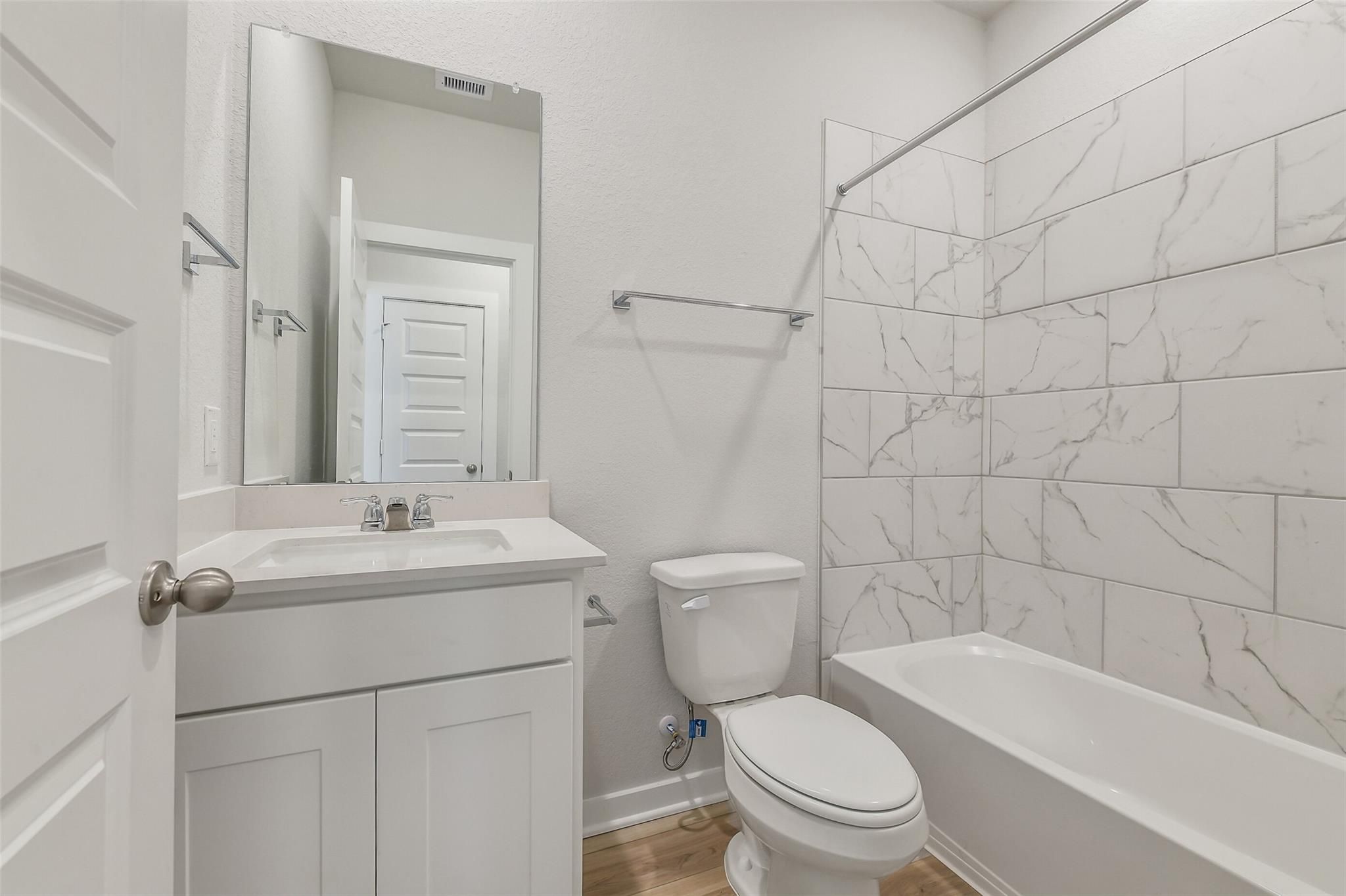 Modern guest bathroom featuring white marble-look tile tub surround, vanity sink, and toilet in Davidson Homes San Marcos E, Conroe TX