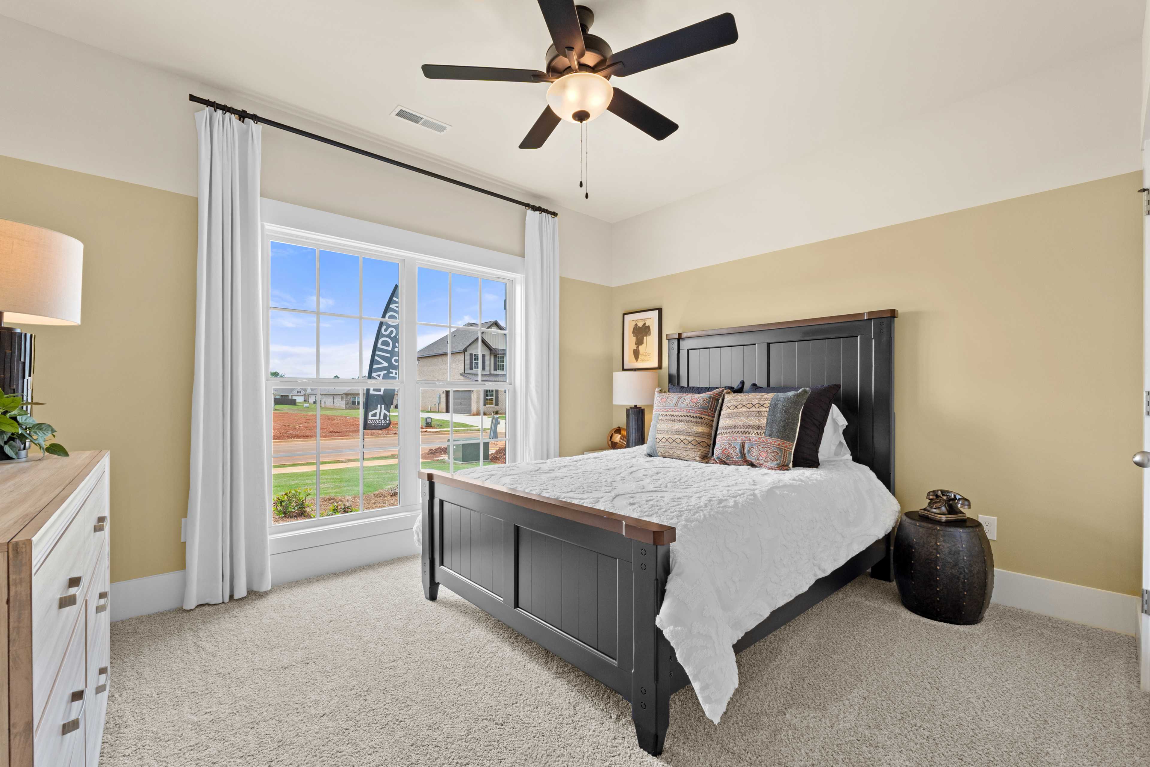 Spacious bedroom at Ivy Hills in Toney Alabama with wooden bed, white bedding, large window overlooking yard, and ceiling fan