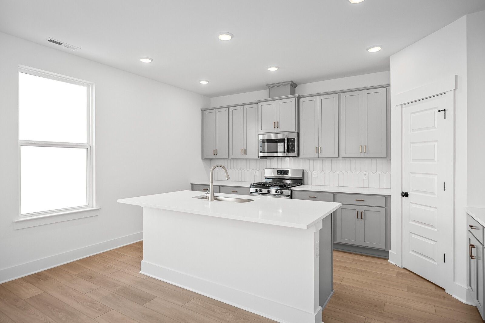 Bright modern kitchen with white island, gray shaker cabinets, stainless appliances, subway tile in The Logan C by Davidson Homes, Gallatin TN