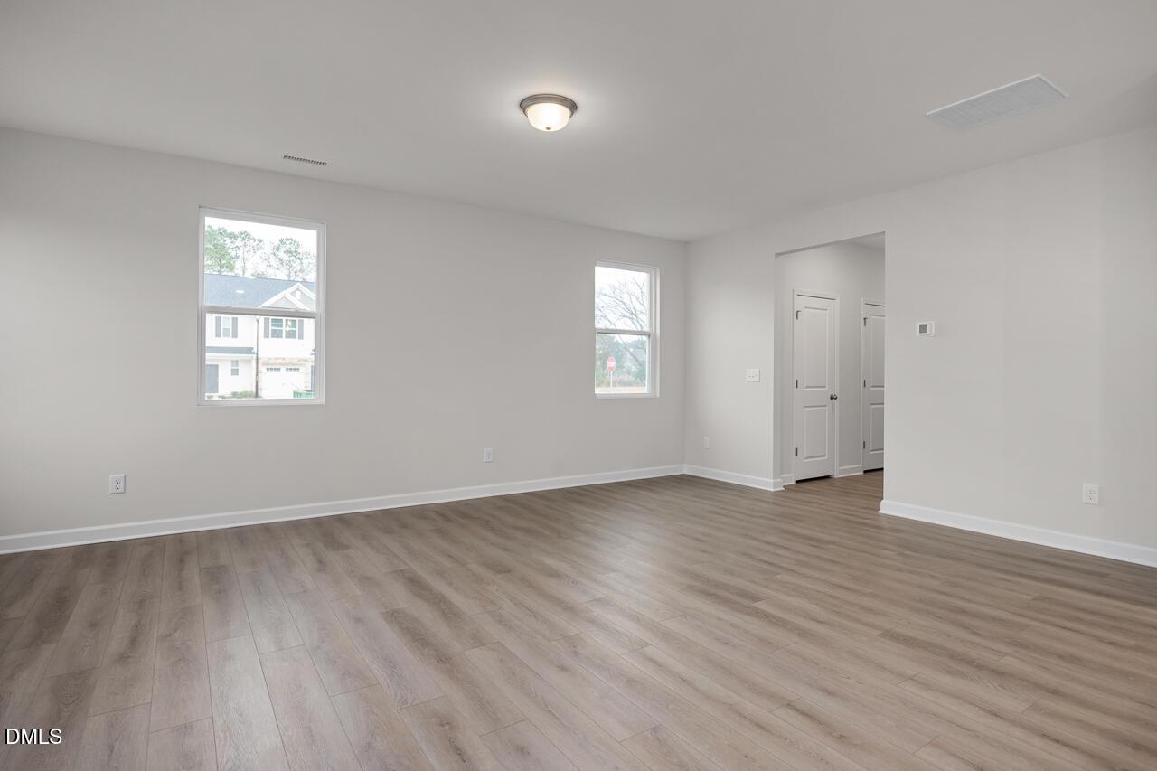Spacious empty living room with light hardwood floors, large windows, and neutral walls in Davidson Homes The Gavin B, Lillington, NC