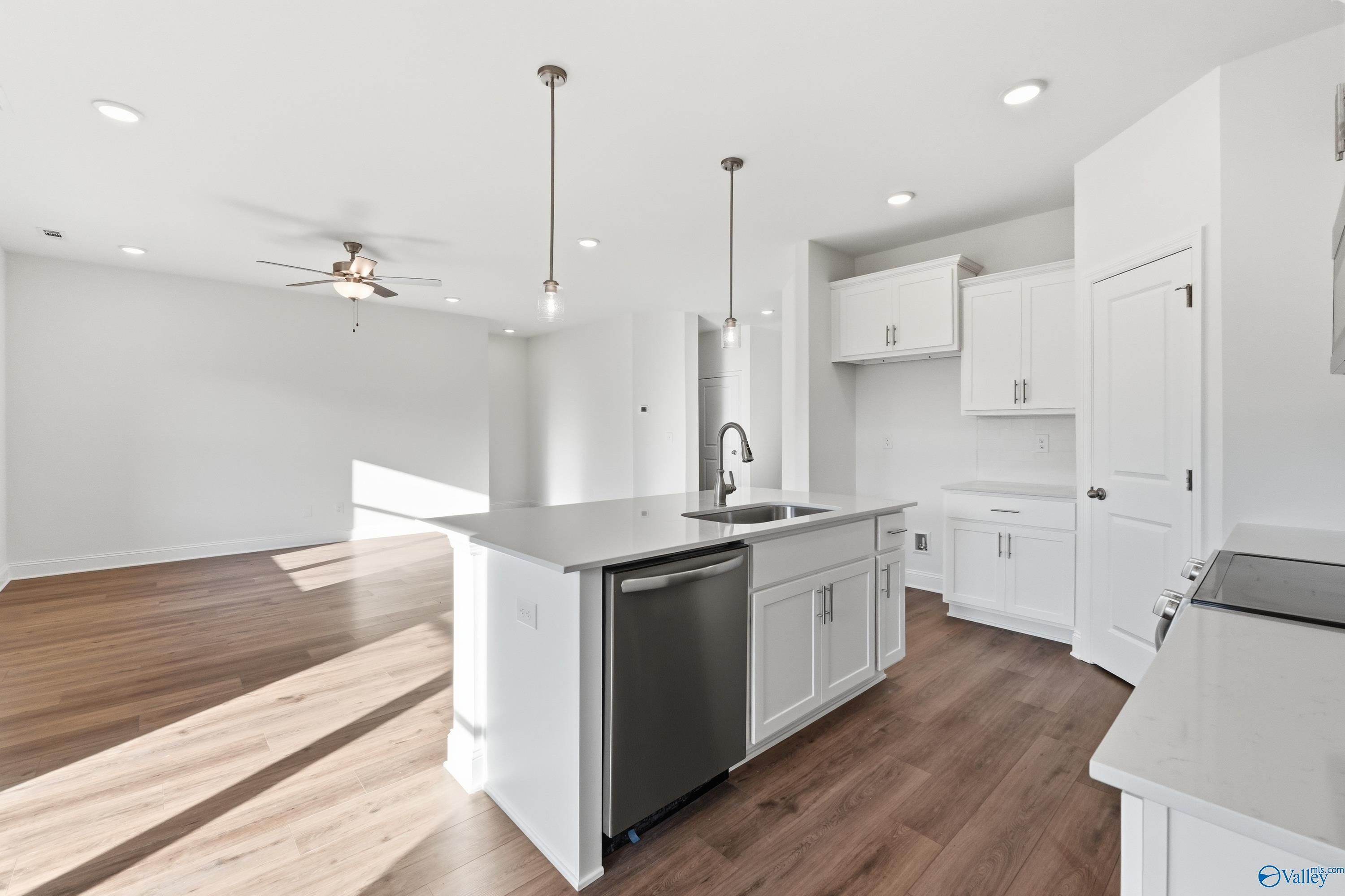 Modern white kitchen with large island, stainless sink and dishwasher, open to living room in The Asheville C, Meridianville AL