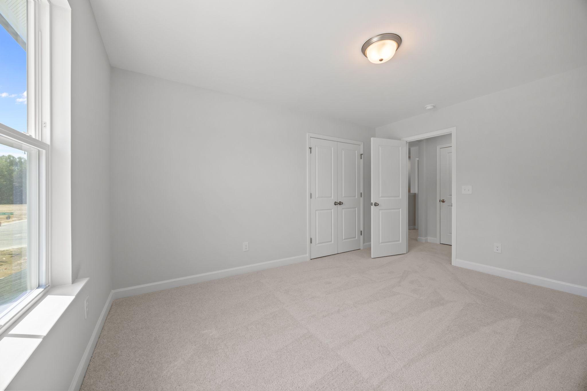 Bright bedroom with neutral carpet and closet doors in The Ashport B floor plan by Davidson Homes.