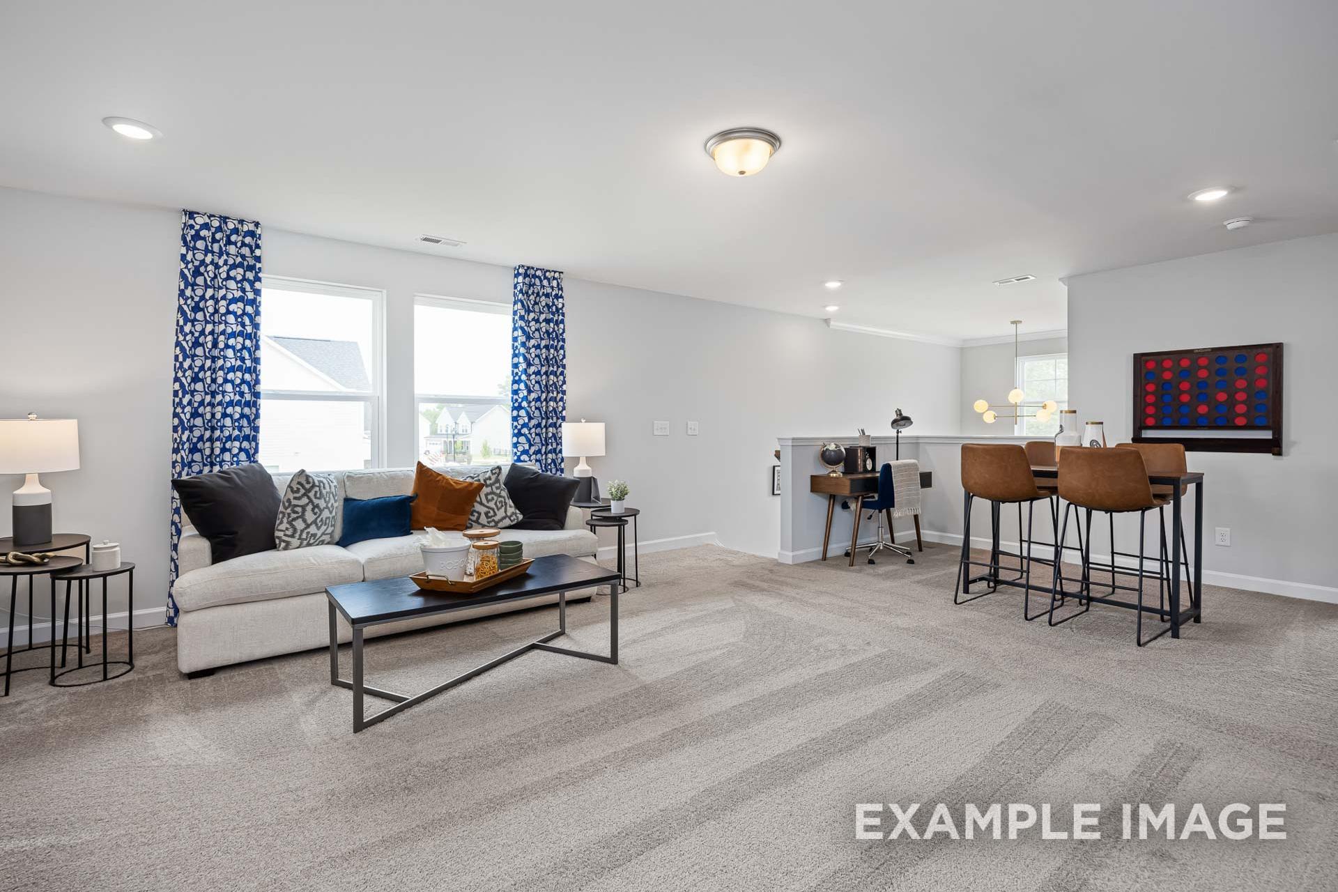 Spacious loft bonus room with gray carpet, blue curtains, sofa, coffee table, and desk bar stools at Woodland Crossing in Zebulon, NC
