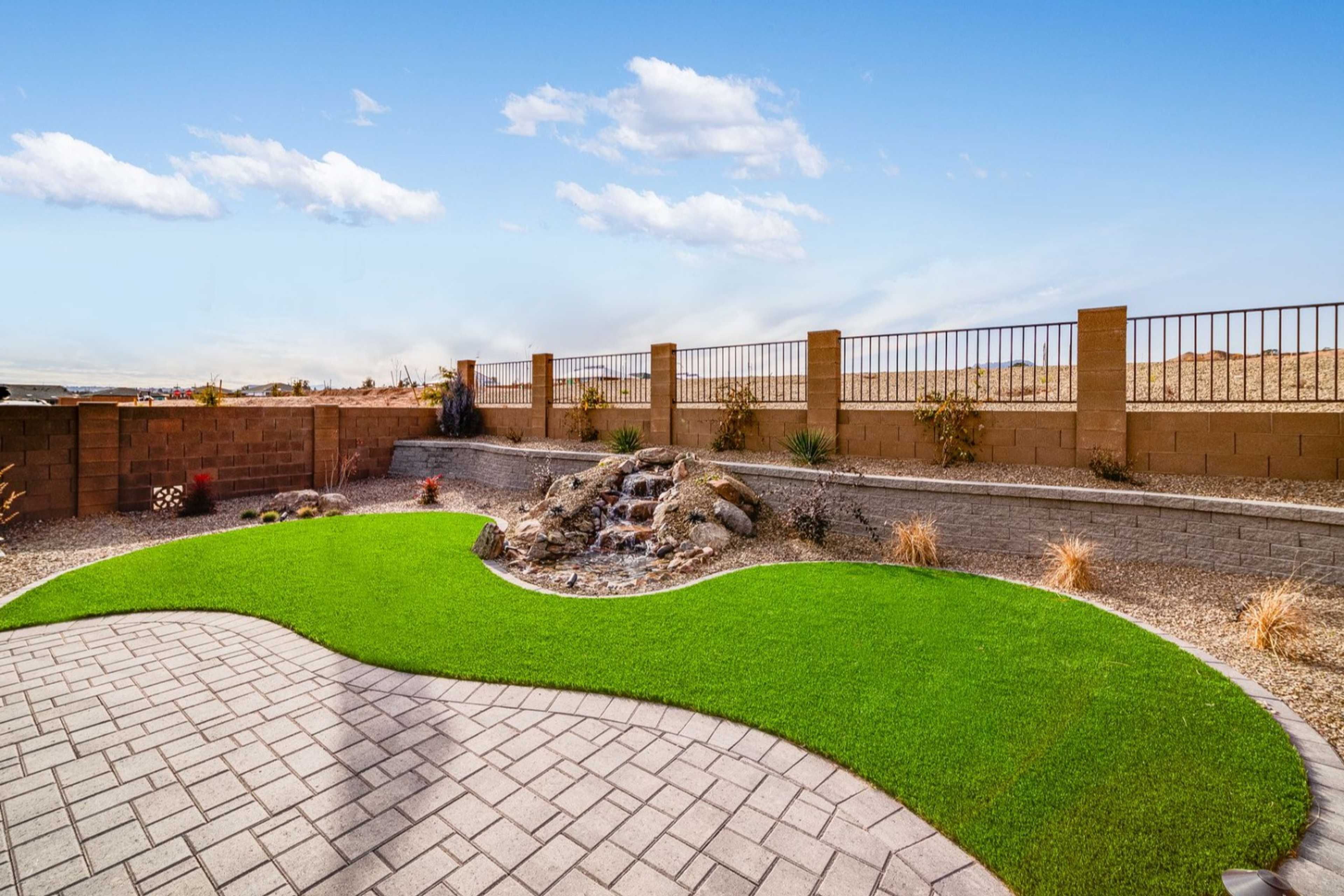 Desert backyard patio with curved synthetic grass, rock waterfall, and paver walkways at South Ranch in Prescott AZ by Davidson Homes