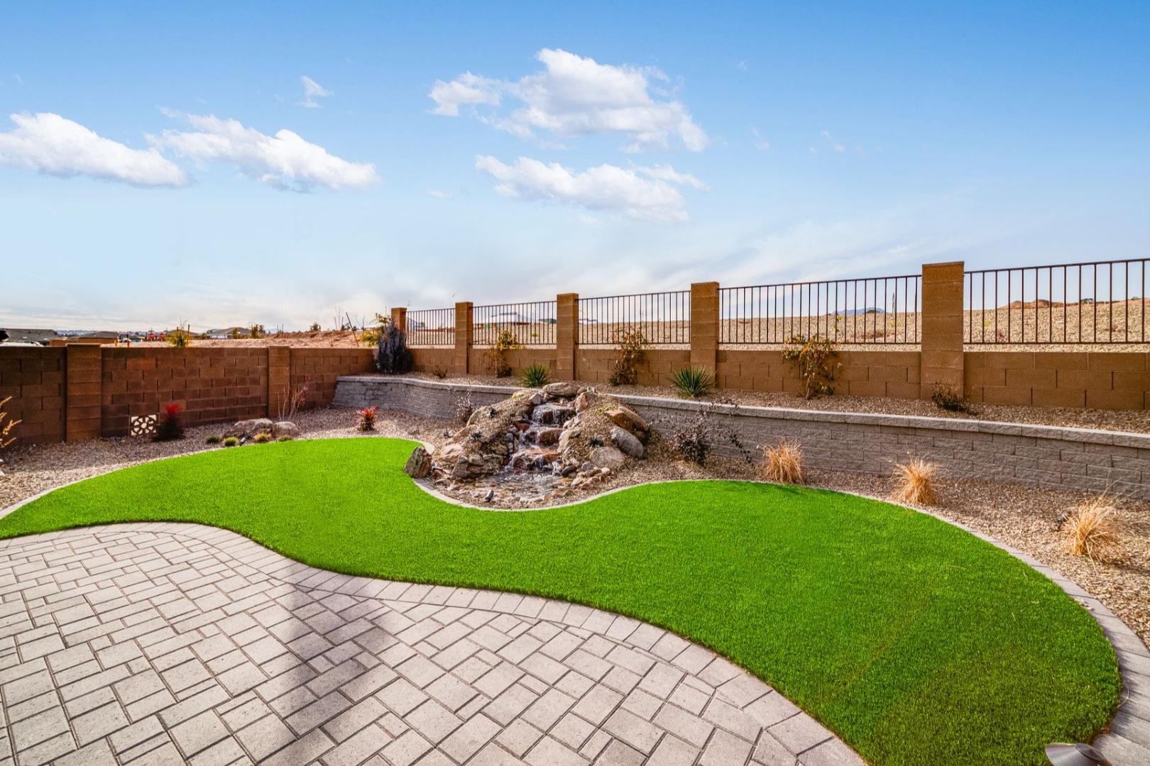 Desert backyard patio with curved synthetic grass, rock waterfall, and paver walkways at South Ranch in Prescott AZ by Davidson Homes