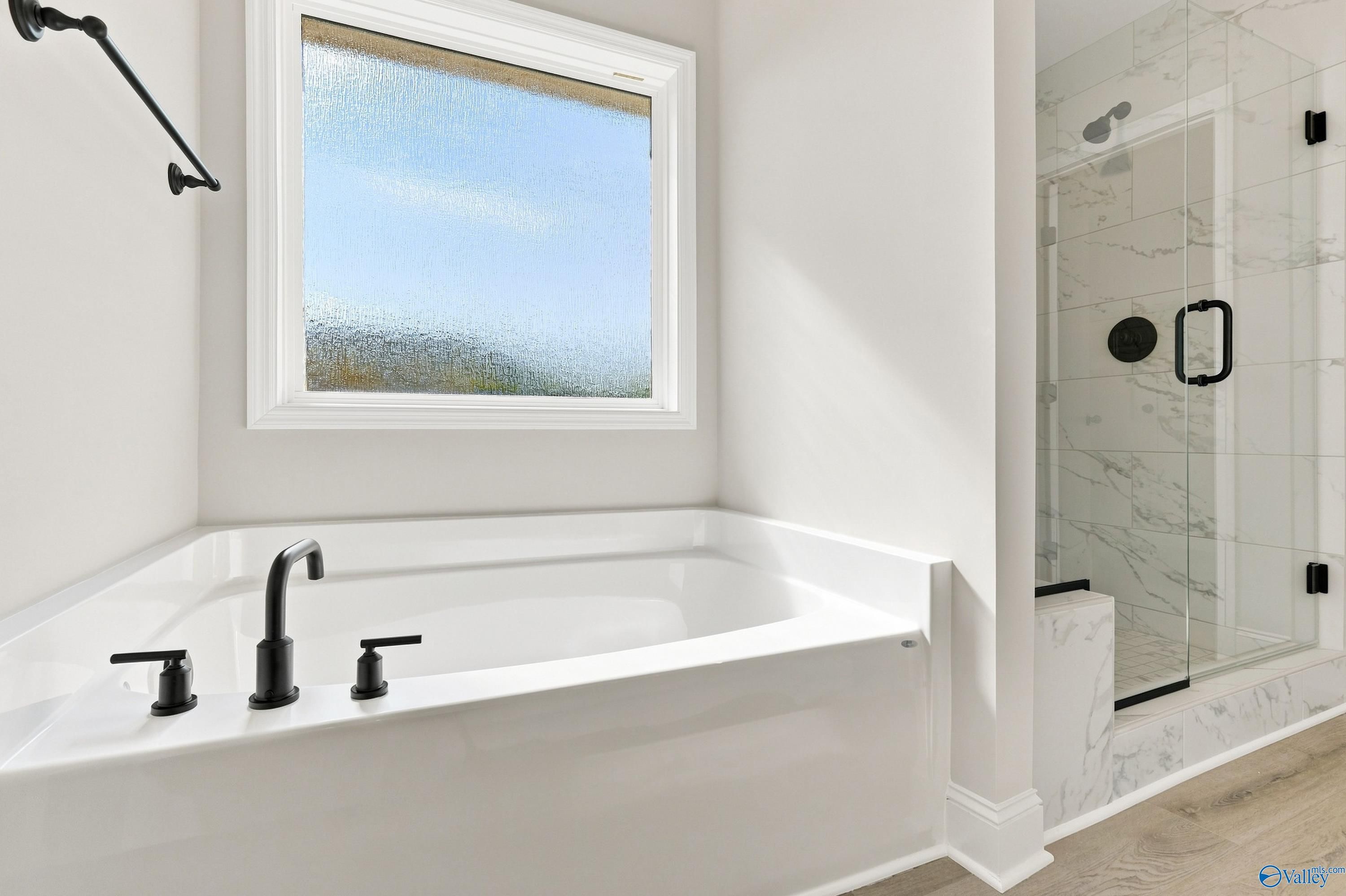Corner soaking tub with matte black fixtures beside marble walk-in shower in Davidson Homes Chelsea B master bath, New Market, AL