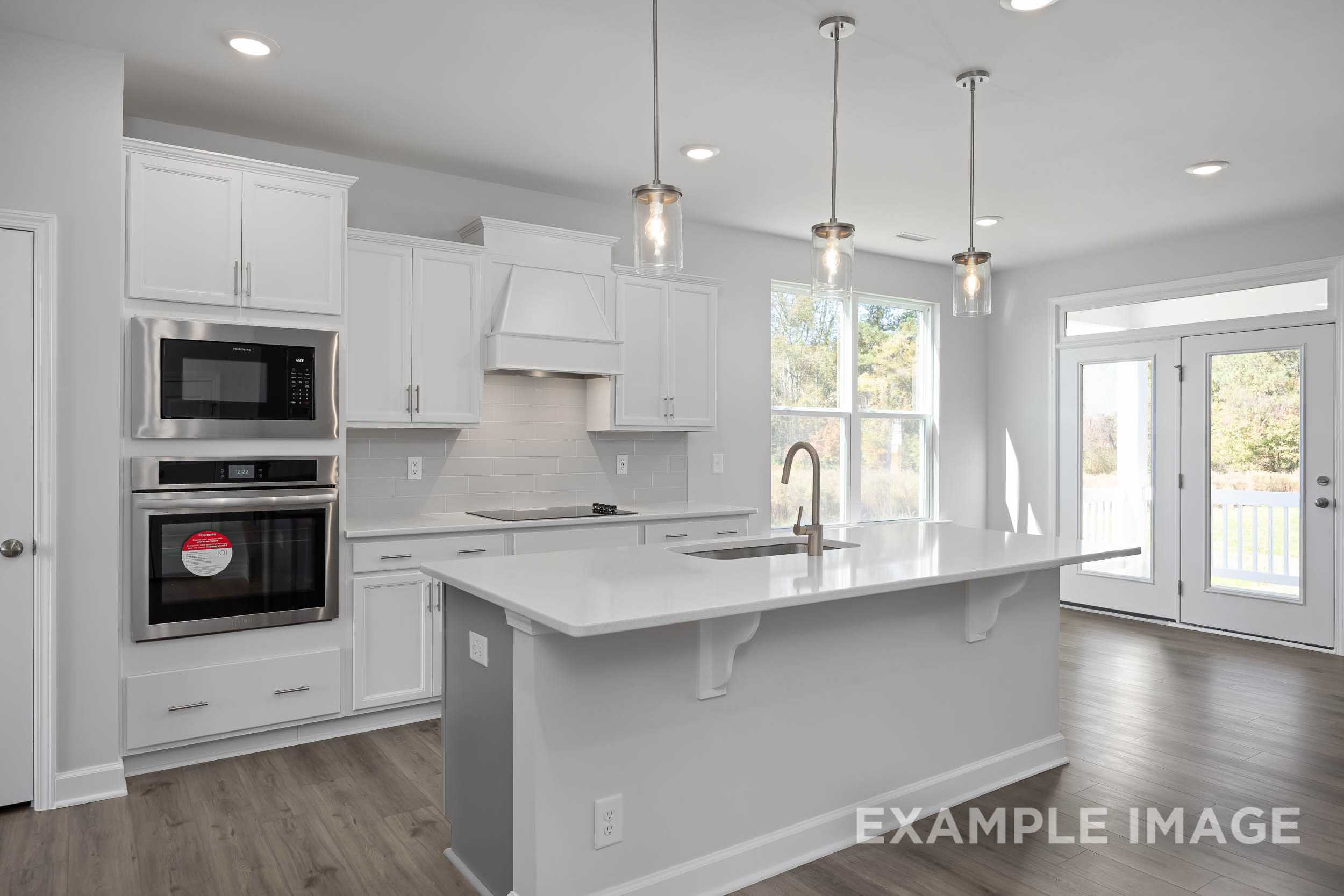 Modern kitchen in The Ash by Davidson Homes featuring white shaker cabinets, large island sink, stainless double oven, and French doors