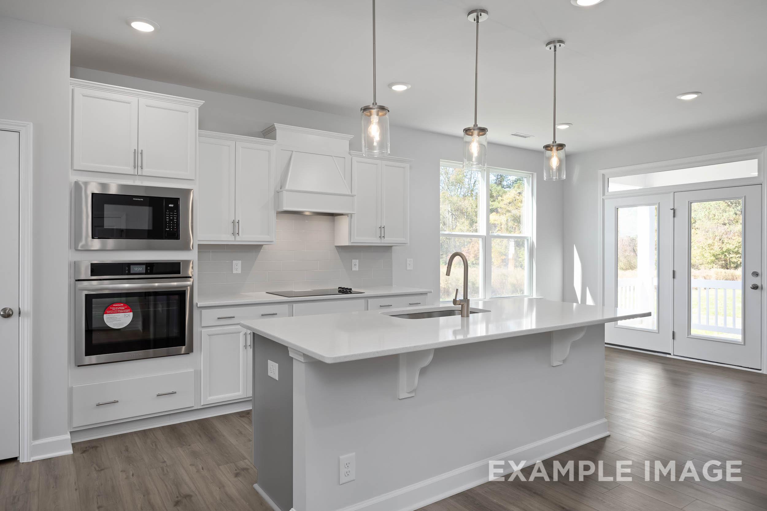 Modern kitchen in The Ash by Davidson Homes featuring white shaker cabinets, large island sink, stainless double oven, and French doors