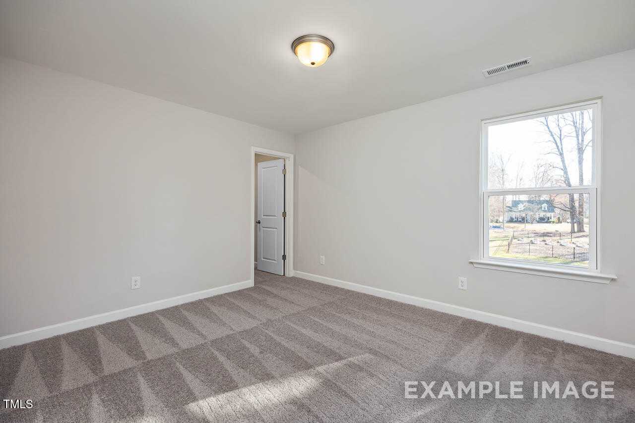 Bright secondary bedroom with neutral walls, carpet flooring, and large window in Davidson Homes Hickory II B, Lillington, NC