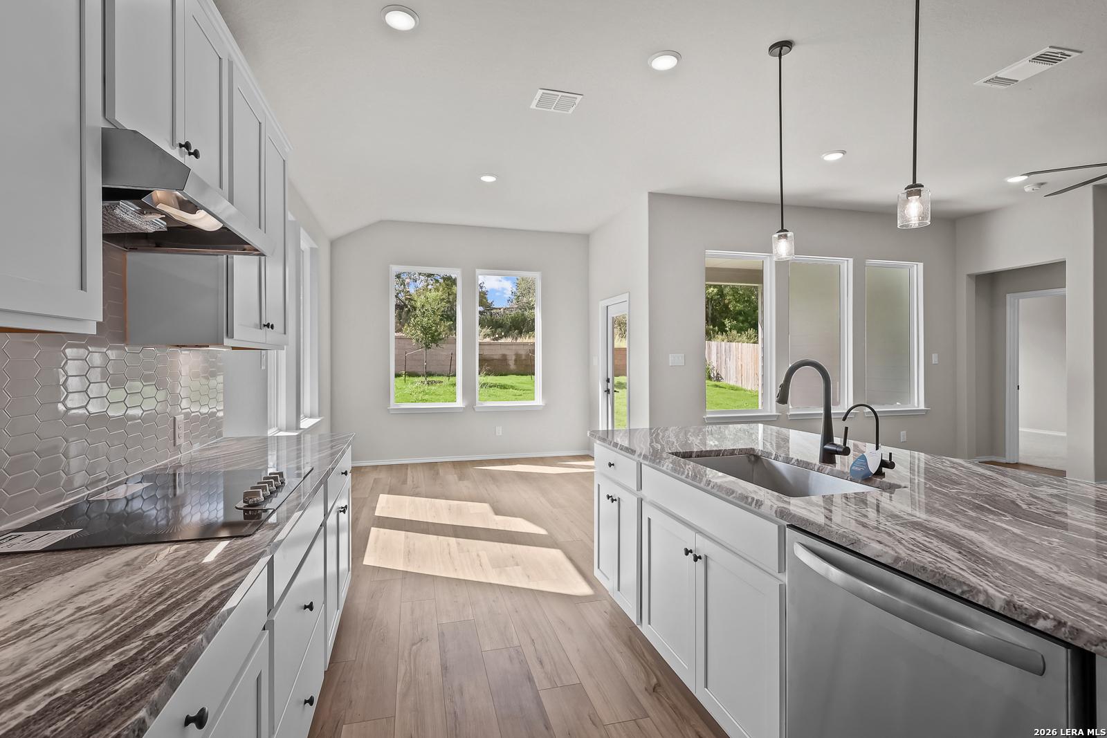 Bright kitchen with white cabinetry, granite island, and hexagon tile backsplash in Davidson Homes' The Sequoia C, Royal Crest, San Antonio