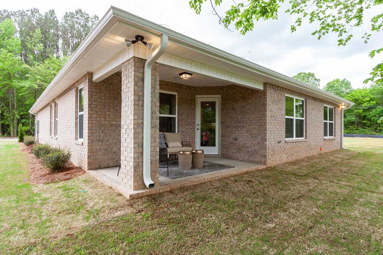 Side view of The Franklin 1-story home by Davidson Homes, brick exterior with covered patio, seating, and greenery in Meridianville AL