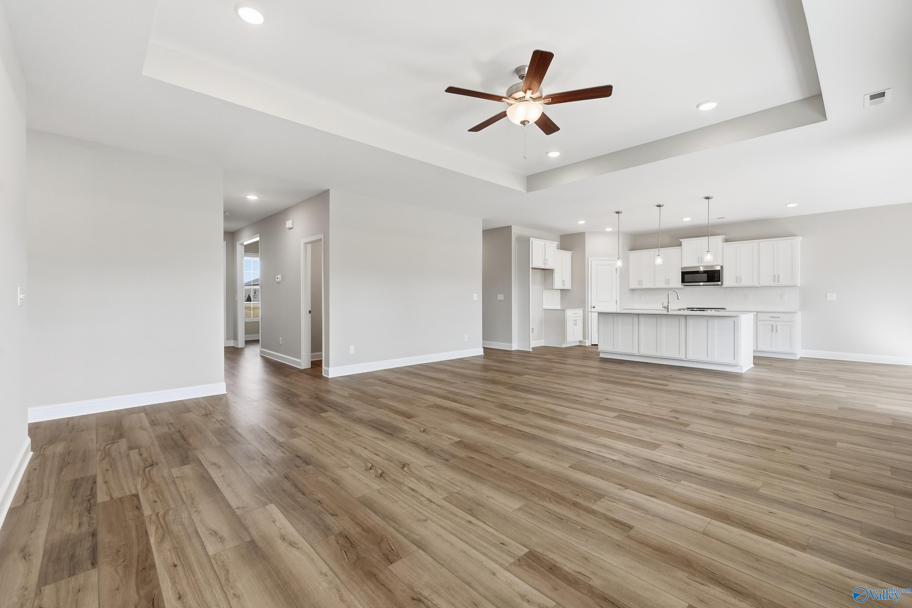 Open-concept living kitchen with hardwood floors, white shaker cabinets, island, and ceiling fan in Davidson Homes The Rockford, Harvest AL