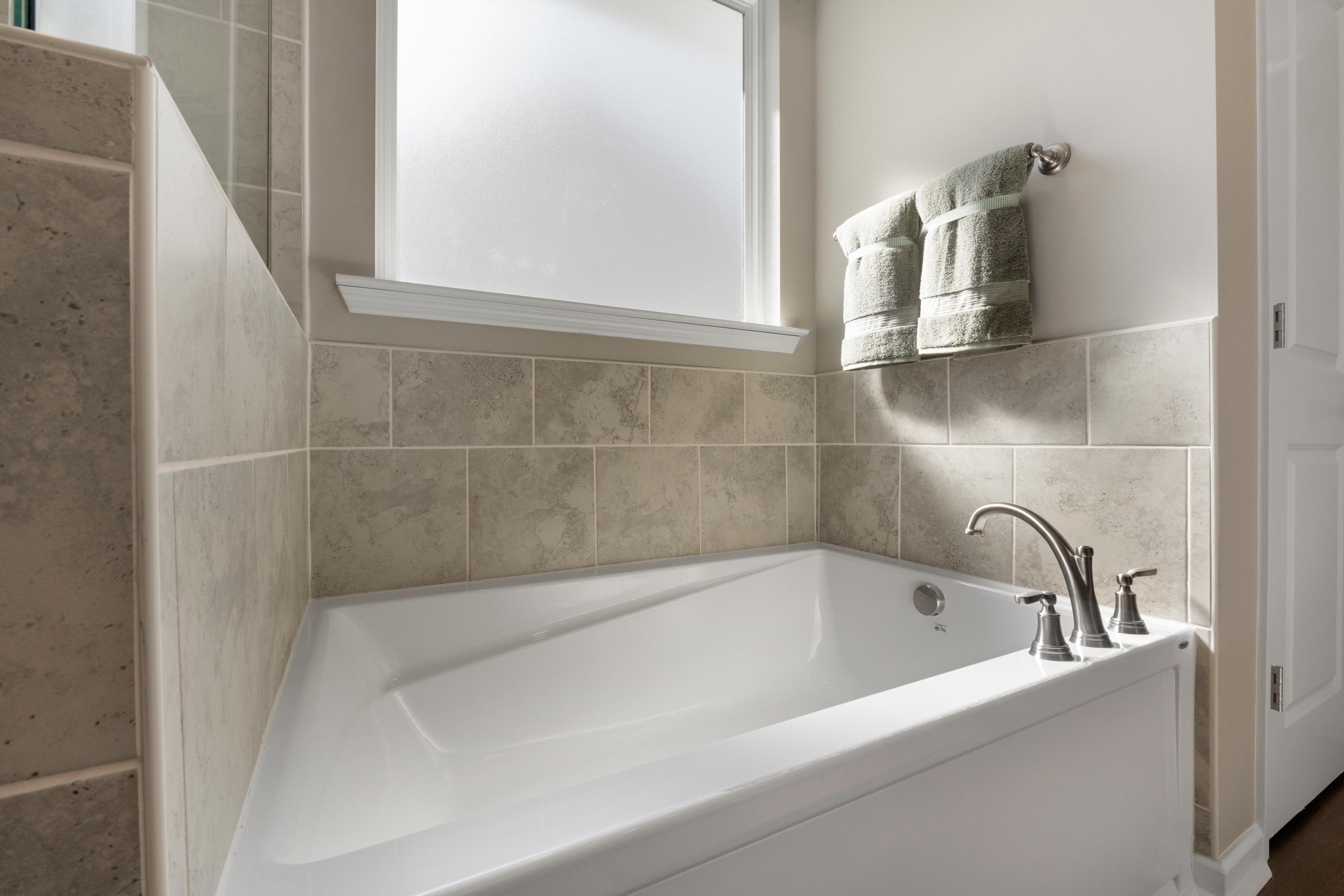 Spacious corner soaking tub in Evergreen Mill bathroom, Madison AL by Evermore Homes with beige subway tiles and window