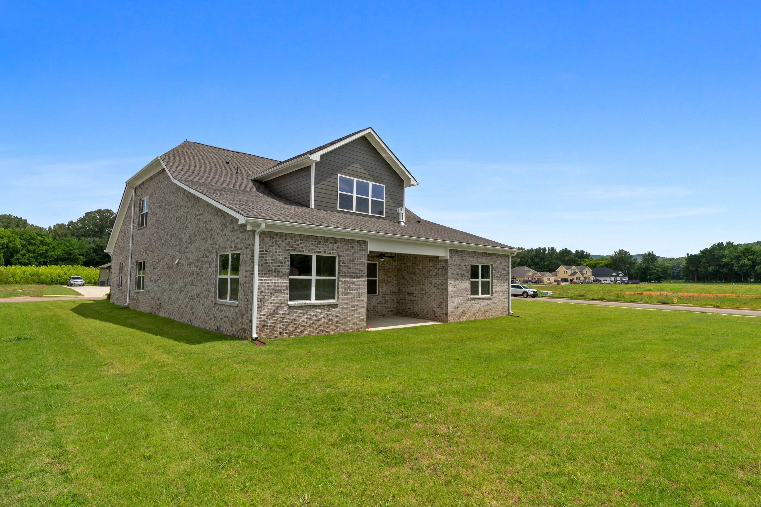 Two-story Oxford A home elevation with gray siding, brick accents, covered porch, and lush green lawn in Owens Cross Roads