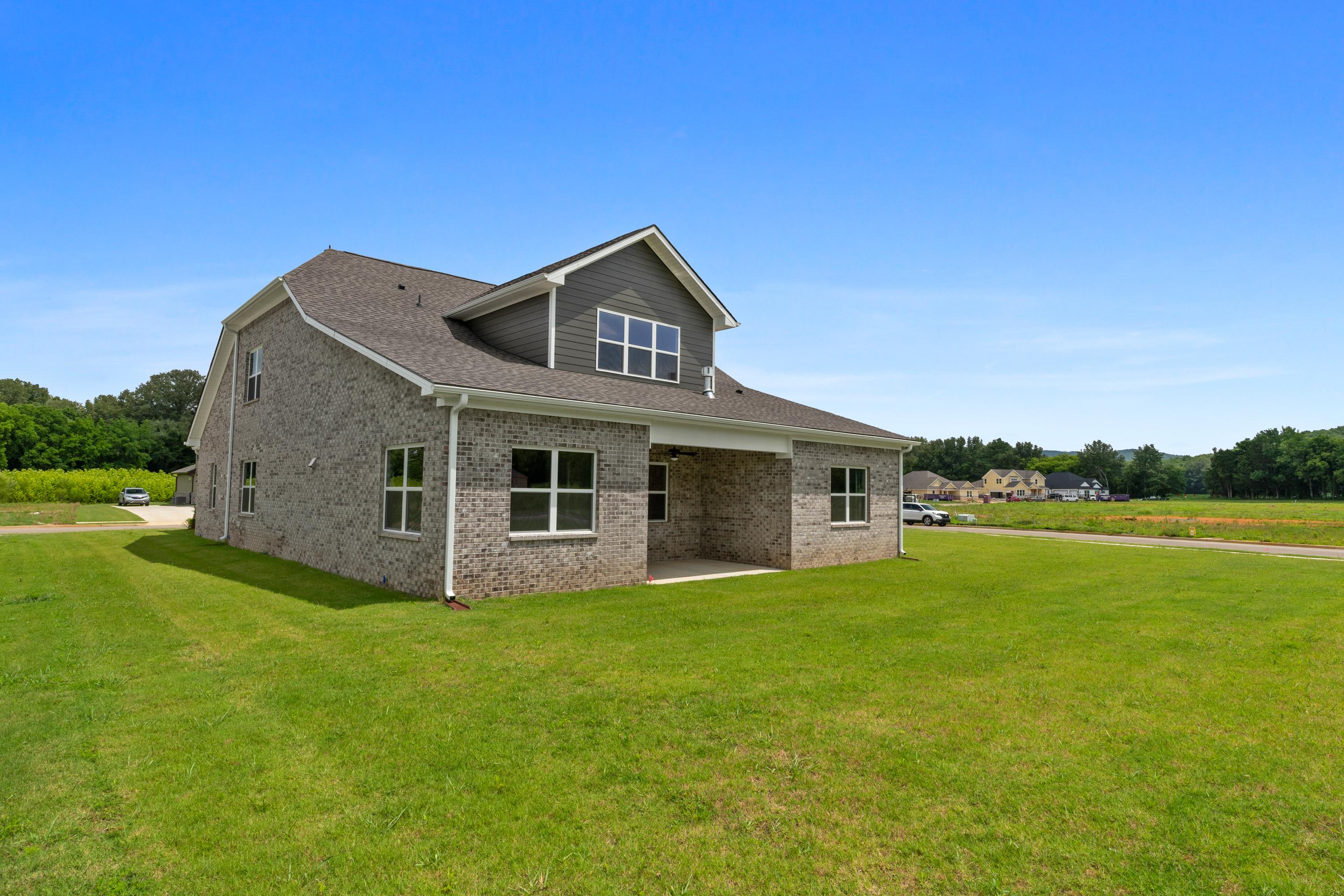 Two-story Oxford A home elevation with gray siding, brick accents, covered porch, and lush green lawn in Owens Cross Roads