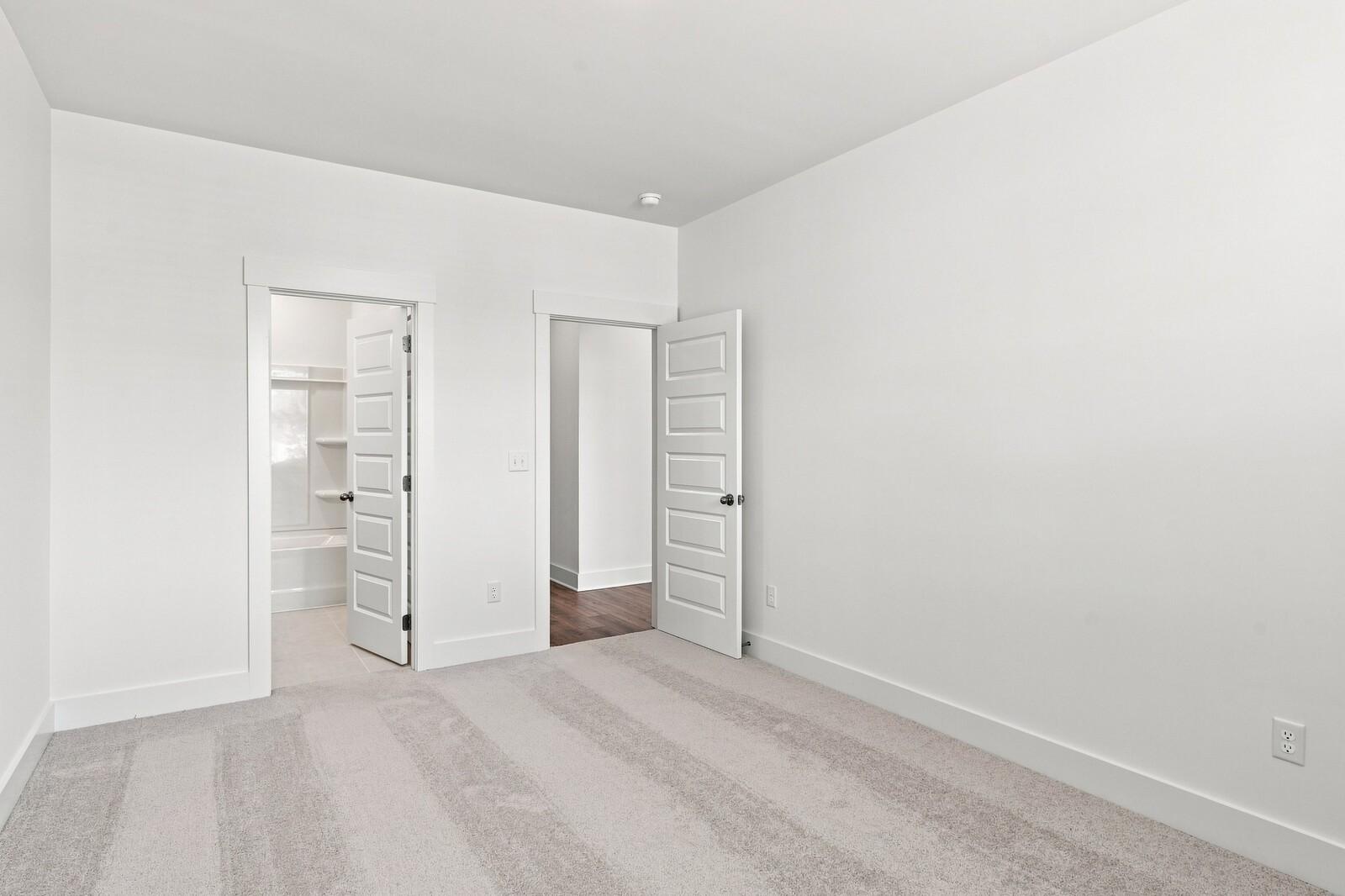 Bright carpeted bedroom with open doors to private bath and hallway in Davidson Homes The Willow C, Woods Crossing, Gallatin, TN
