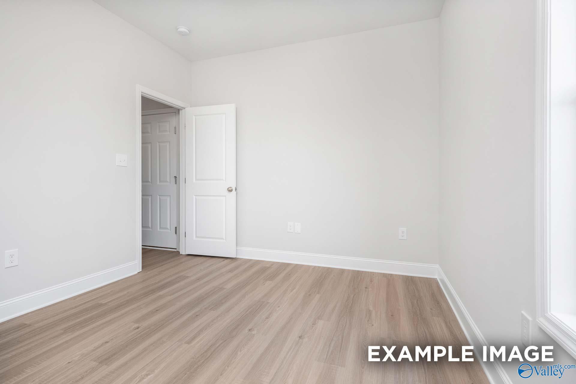 Bright empty bedroom with laminate hardwood floors, white walls, and open door in Davidson Homes The Daphne D, Meridianville, Alabama