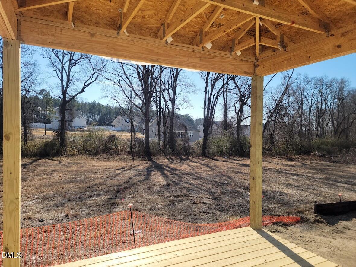 Covered back patio with exposed beams, recessed lights, and safety netting overlooking wooded yard in Davidson Homes The Ashport G, Angier, NC