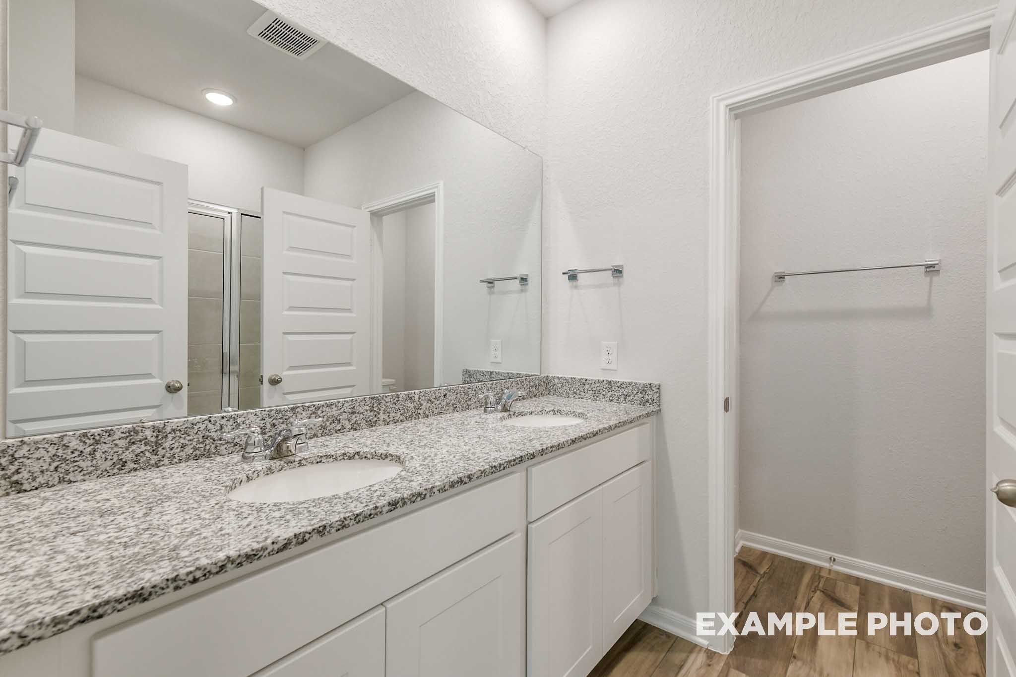 Modern master bathroom in The Frio featuring a dual-sink granite vanity, white cabinetry, and spacious mirror.