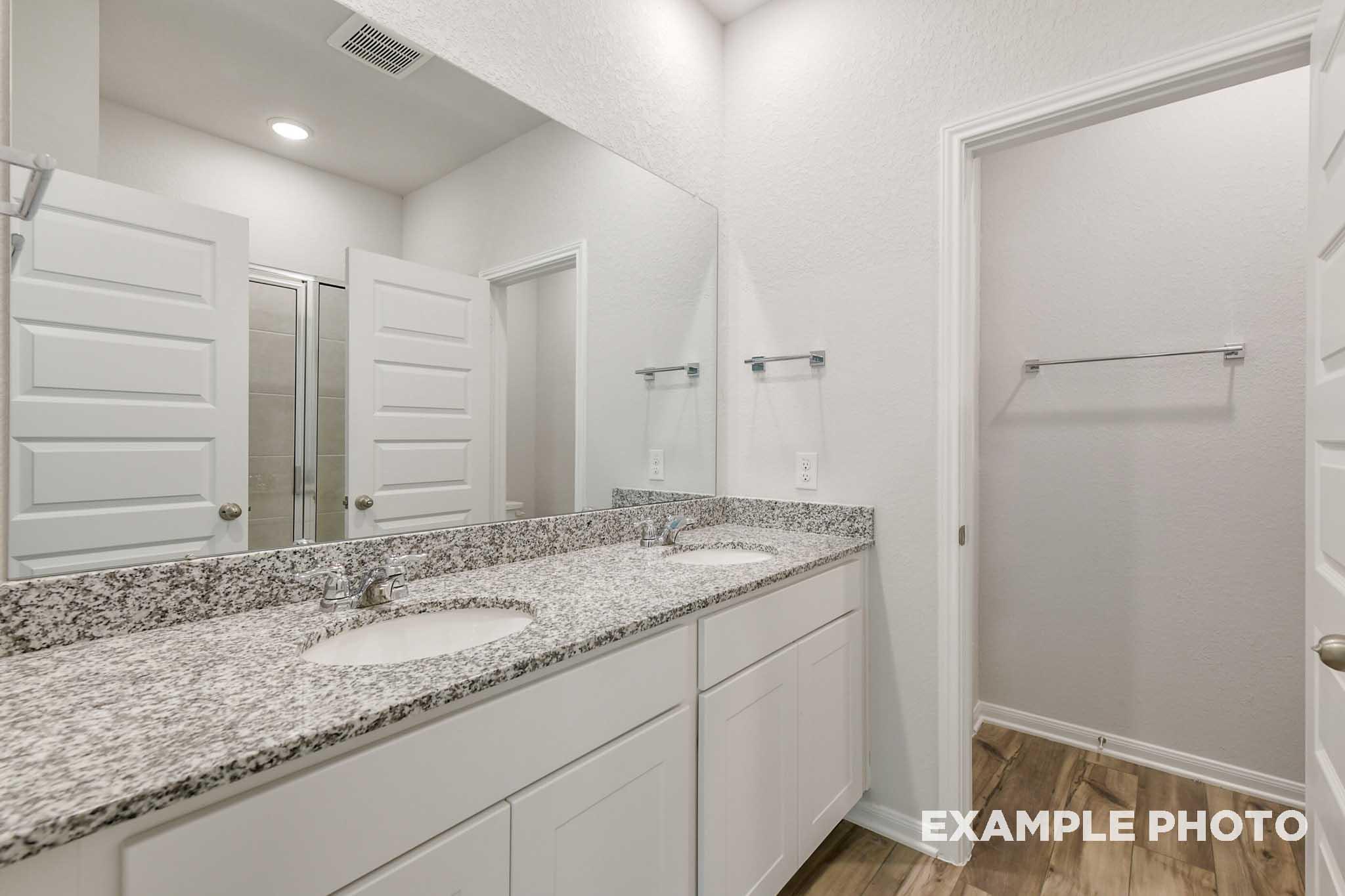 Modern master bathroom in The Frio featuring a dual-sink granite vanity, white cabinetry, and spacious mirror.