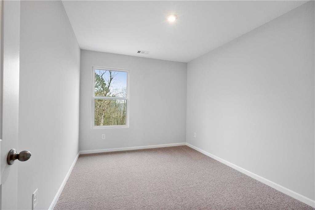Bright secondary bedroom featuring light gray walls, large window with tree view, and beige carpet in Davidson Homes The Durant A, Emerson, Georgia