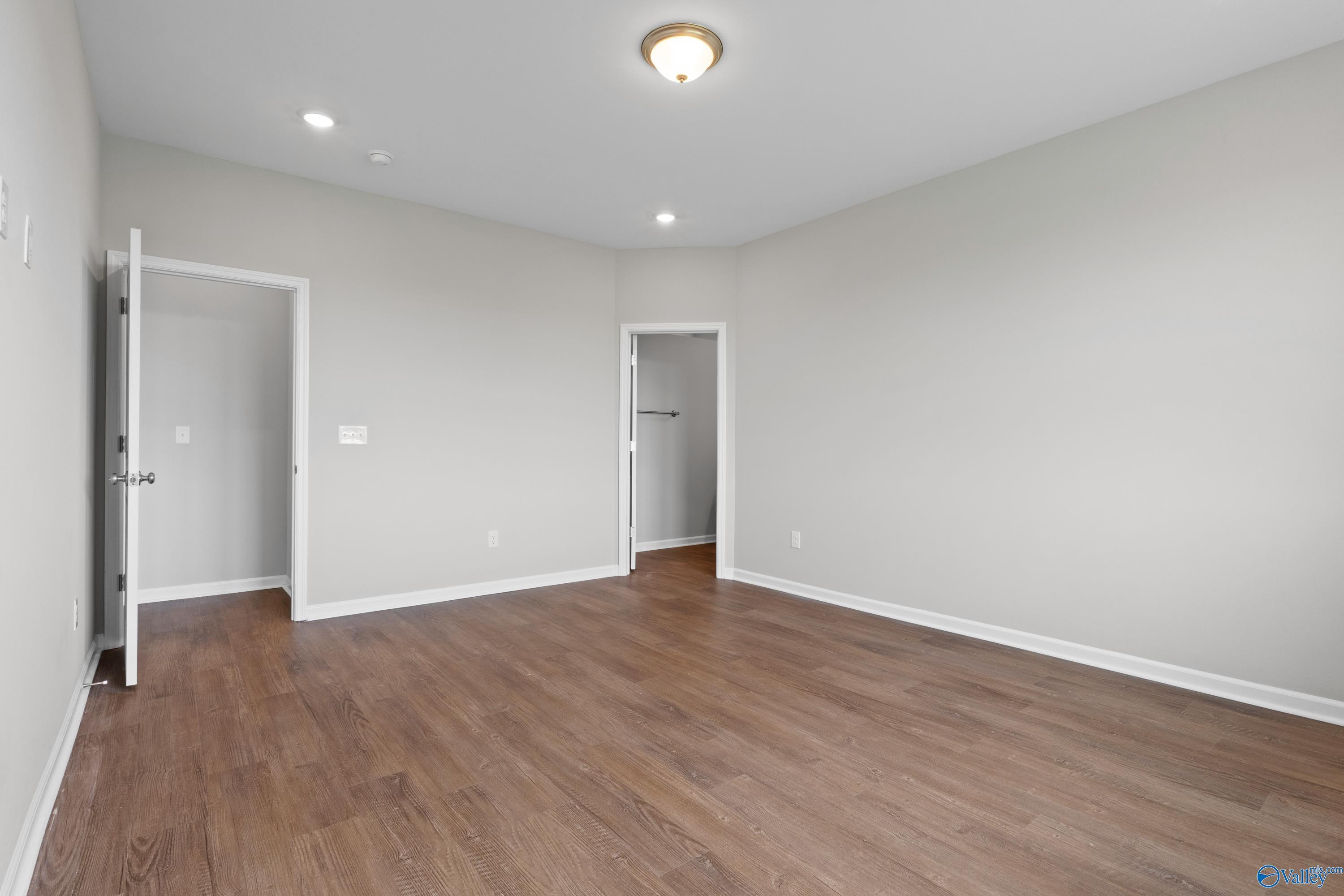 Empty bedroom with light gray walls, hardwood floors, and open doorways in Davidson Homes The Dorado, Athens, Alabama
