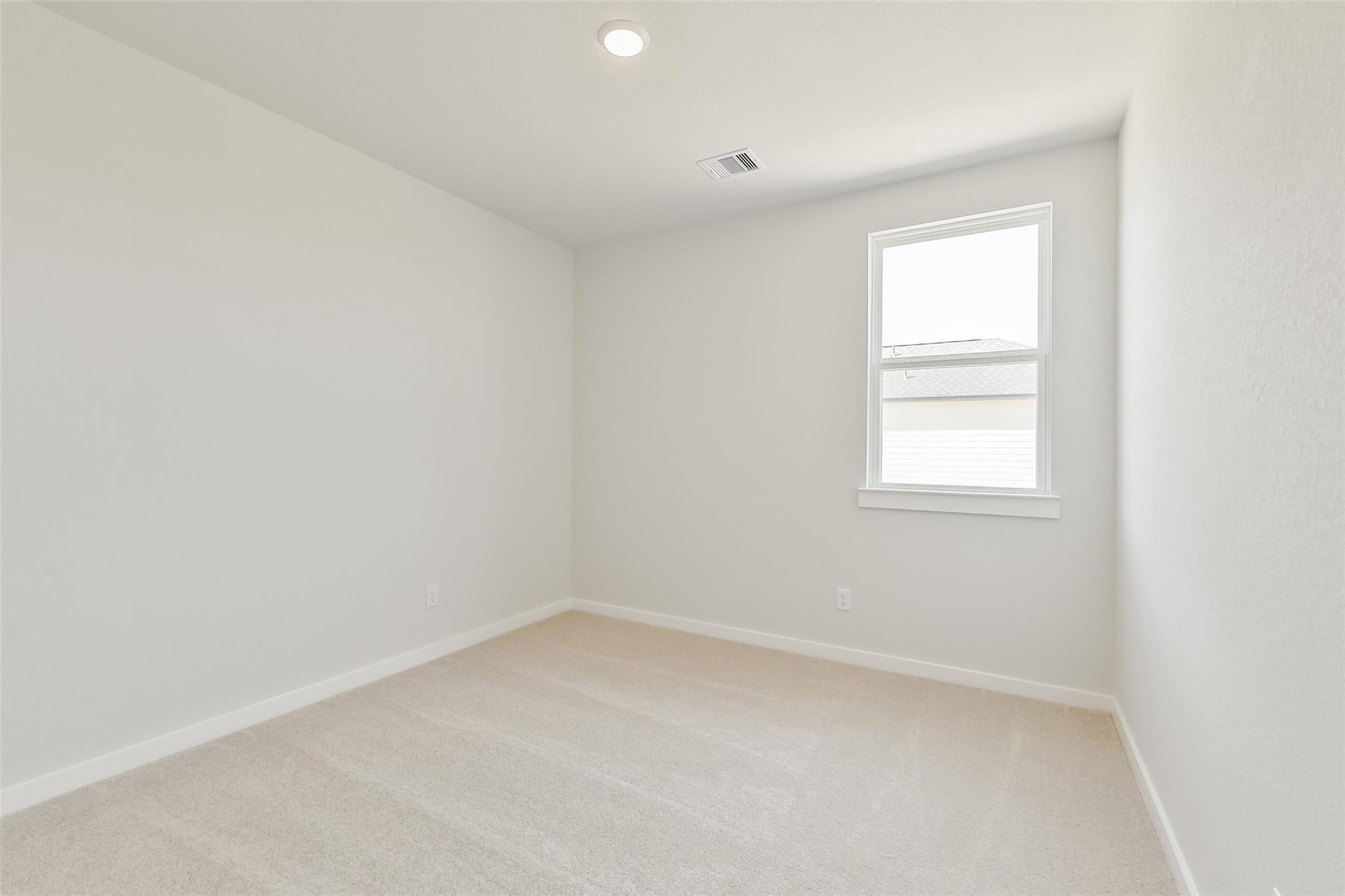 Empty secondary bedroom with neutral white walls, beige carpet, and large window in Davidson Homes The Frio G, Conroe Texas