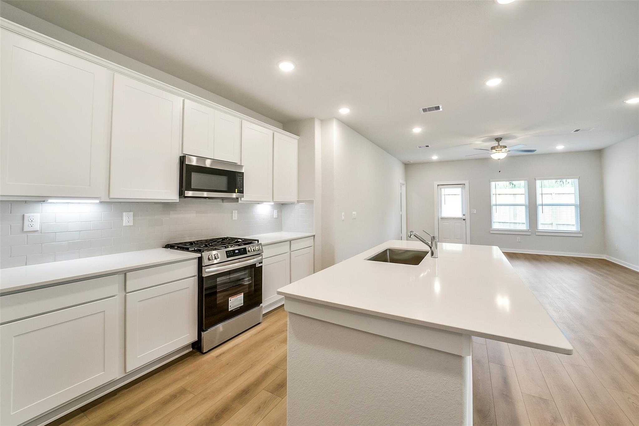 Modern white kitchen with stainless appliances, quartz island, and open layout in Davidson Homes The Blanco E, Magnolia TX