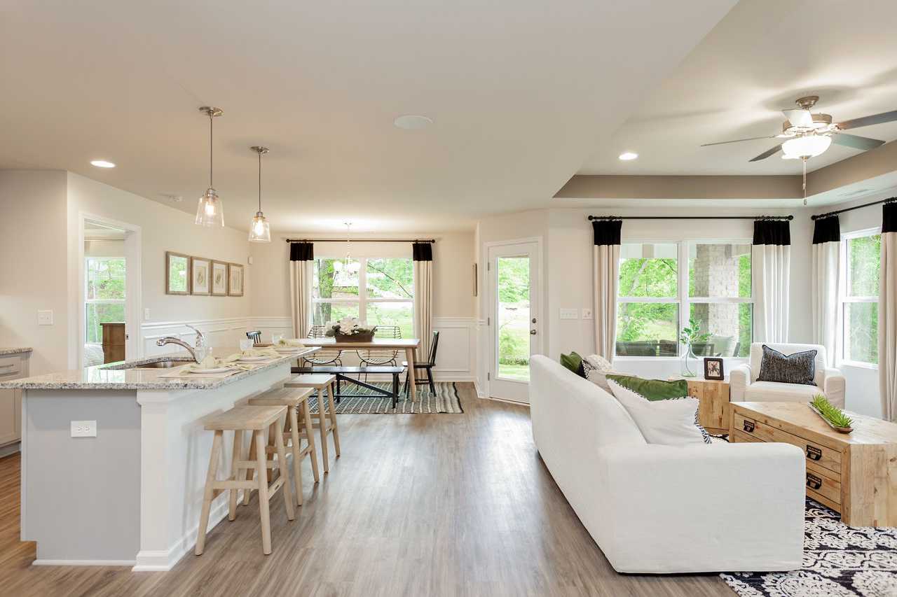Open-concept living and kitchen in The Franklin home with white island, bar stools, dining table, and plush sofa