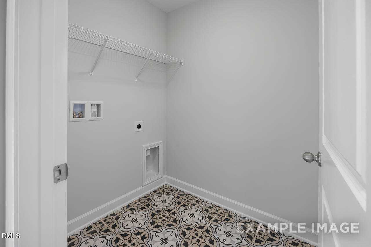 Bright laundry room with open shelving, utility sink, and patterned tile floor in Davidson Homes The Adalynn A, Lillington, NC