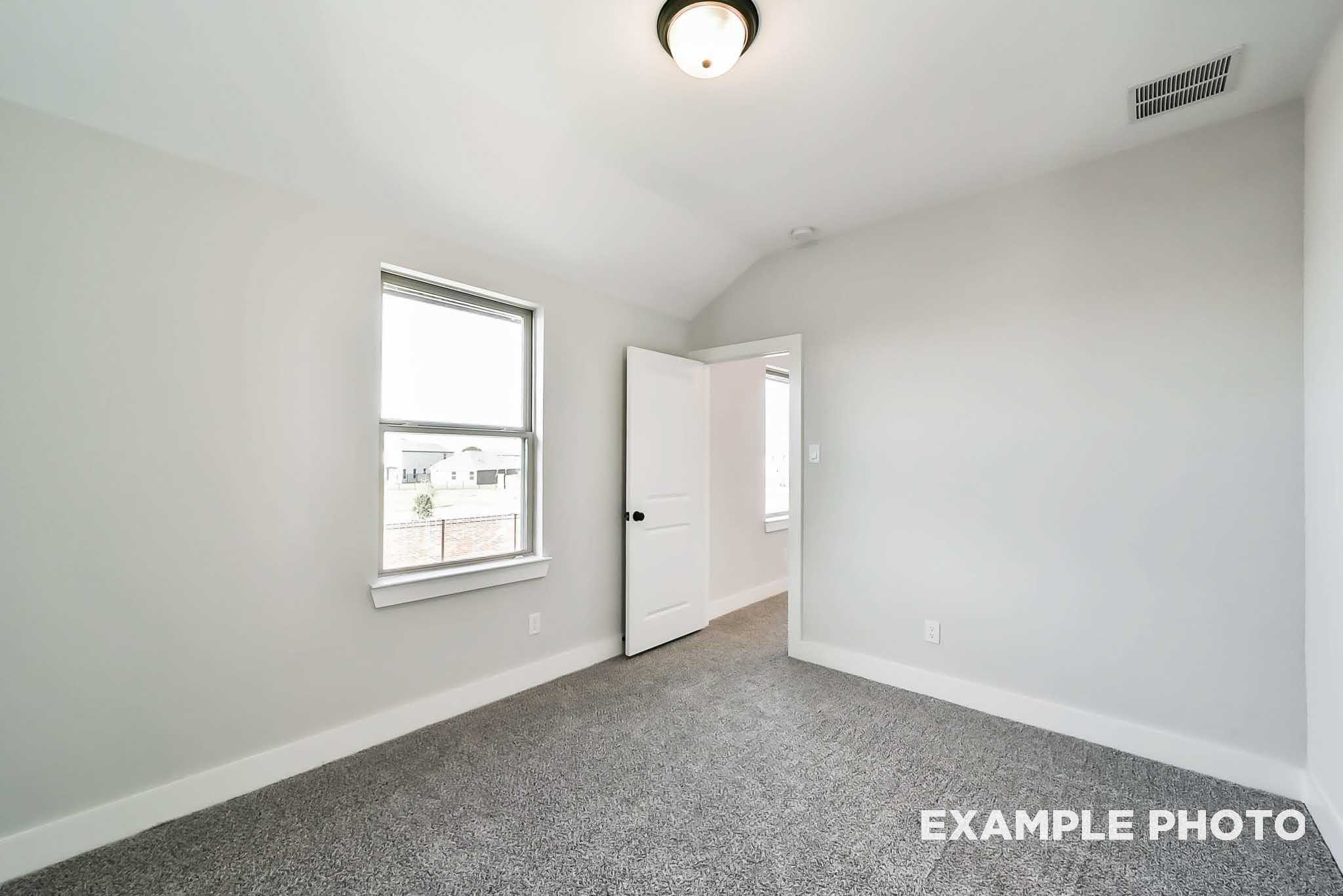 Bright secondary bedroom with large window, open door, and gray carpet in The Philip C 4-bedroom home, Rosharon, Texas