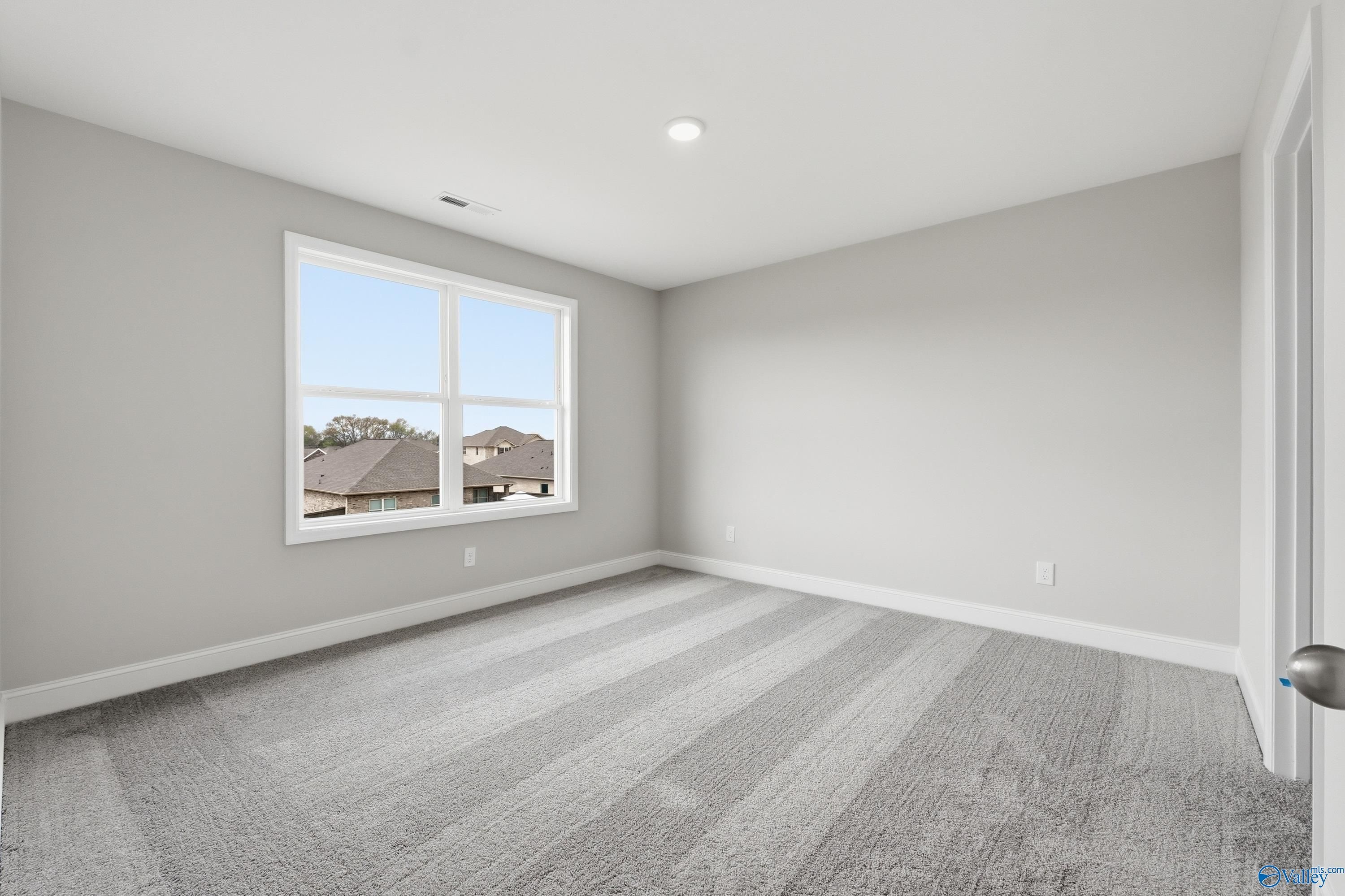 Bright empty bedroom with gray walls, carpet flooring, and large window overlooking neighborhood in Davidson Homes The Shelby B, New Market, Alabama