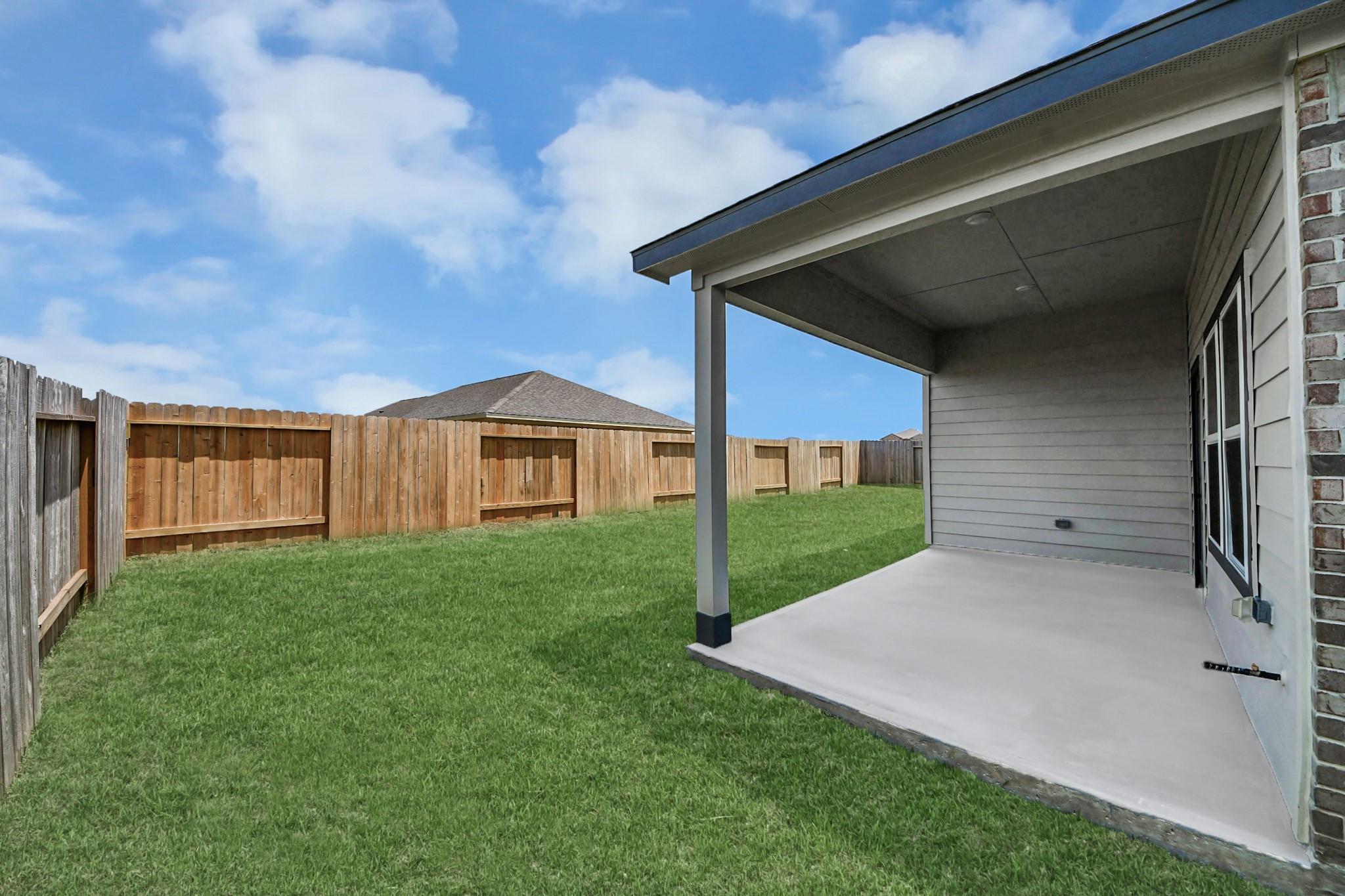 Covered concrete patio overlooking fenced backyard at Davidson Homes The Riviera C in River Ranch Meadows, Dayton, Texas