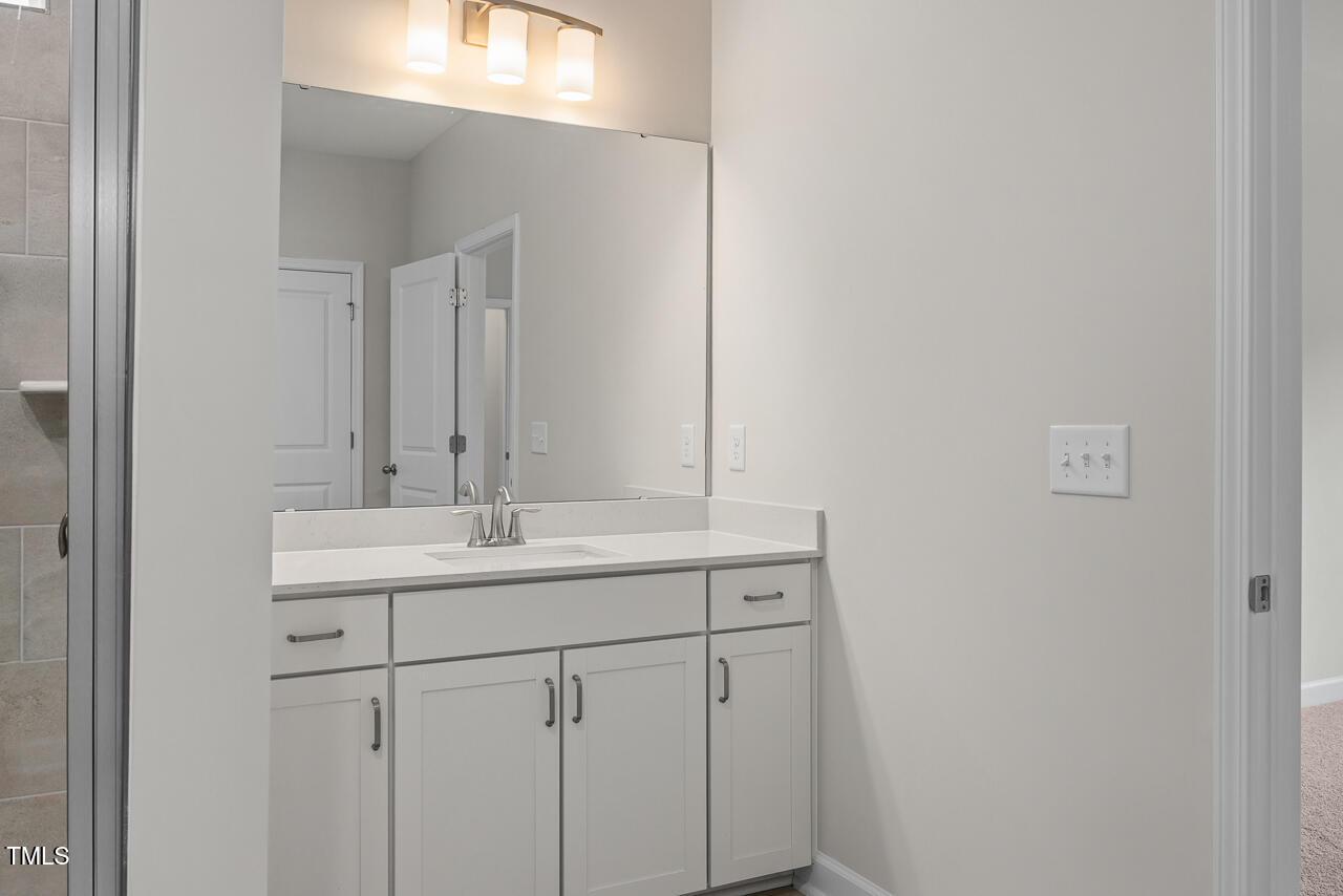 Elegant primary bathroom vanity with white cabinets, single sink, large mirror, and warm lighting in Davidson Homes The Aspen B, Wake Forest, NC