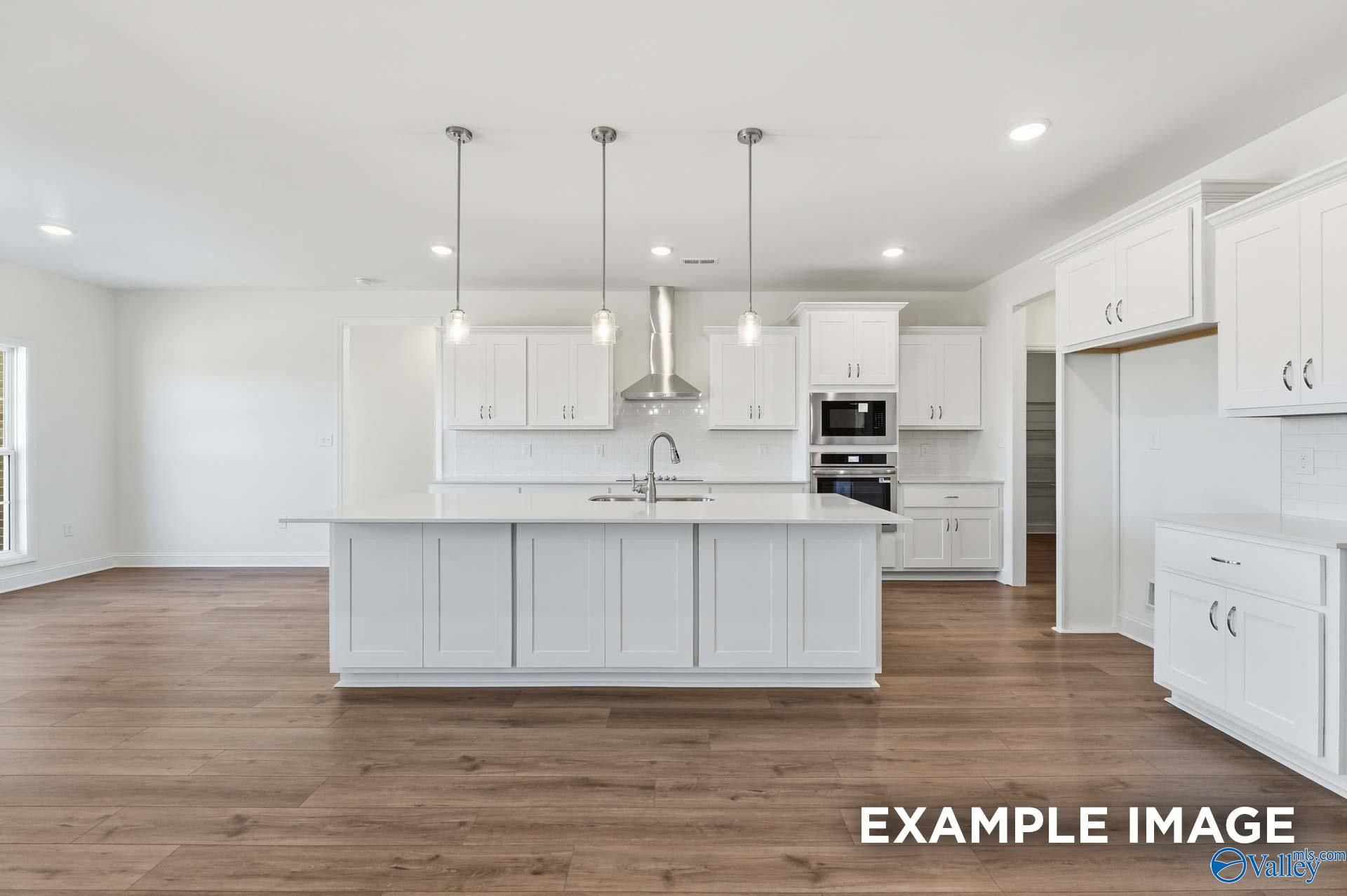 Modern white kitchen with large island and stainless steel appliances in The Valencia floor plan, Briercreek, Meridianville.