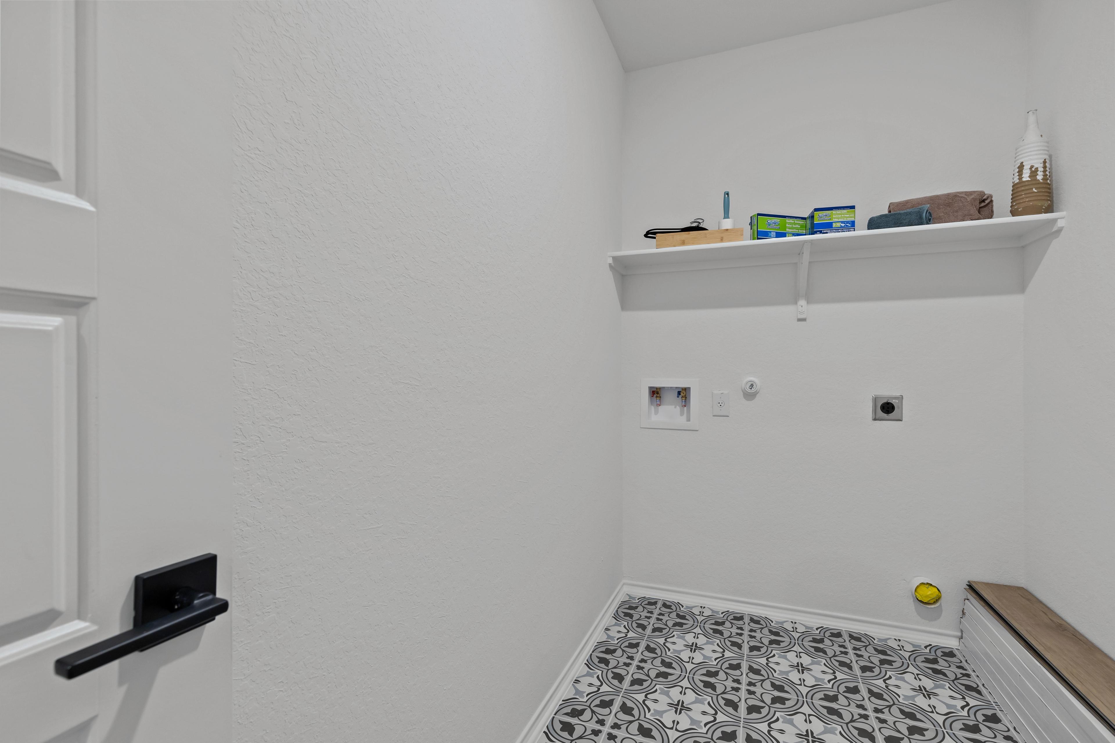 Spacious laundry room in The Douglas F featuring built-in shelves, washer dryer hookups, and patterned tile floor