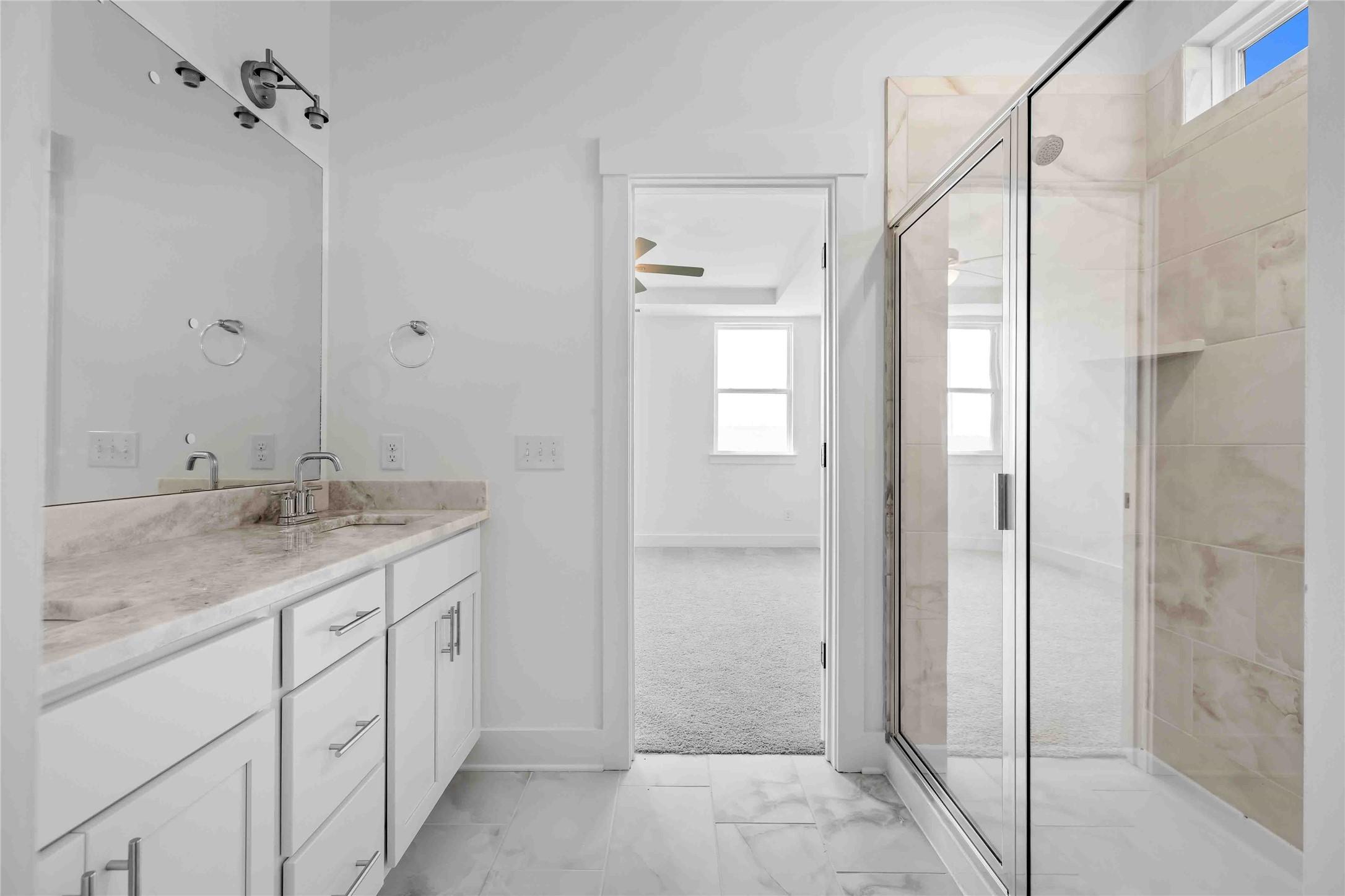 Modern bathroom with white vanity, marble-style countertop, and glass shower in The Ash O floor plan, Heartland, Texas.