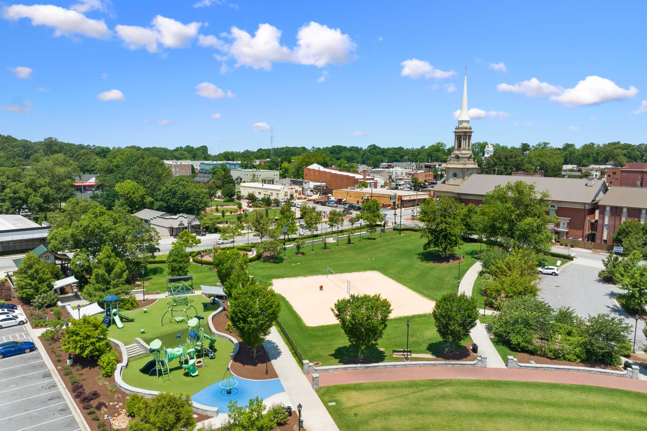 Aerial view of Kelly Preserve playground in Loganville Georgia featuring colorful play structures, sand volleyball court, walking paths and surrounding trees