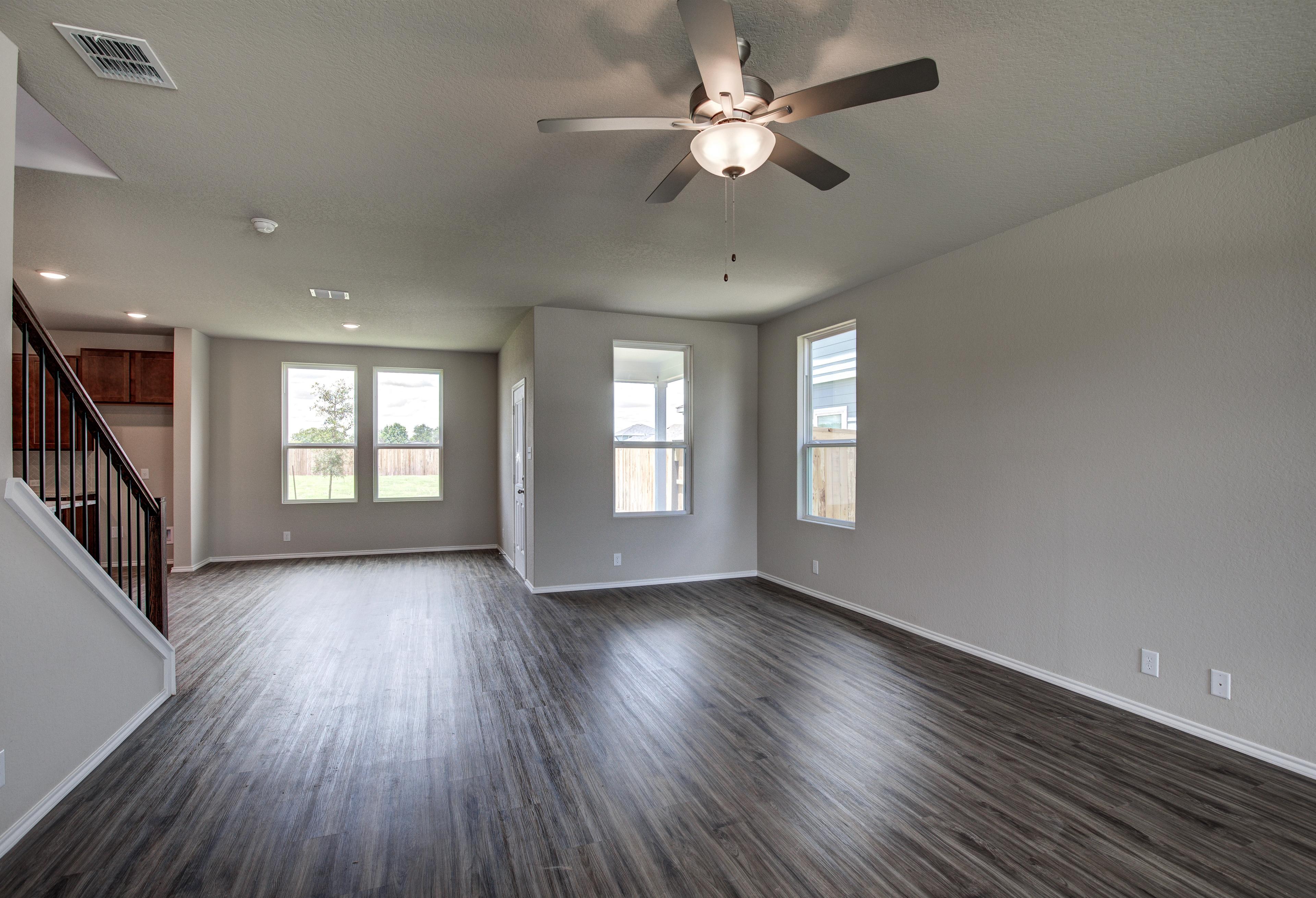 Spacious open-concept living area in The Murray home with hardwood floors, ceiling fan, large windows, and staircase