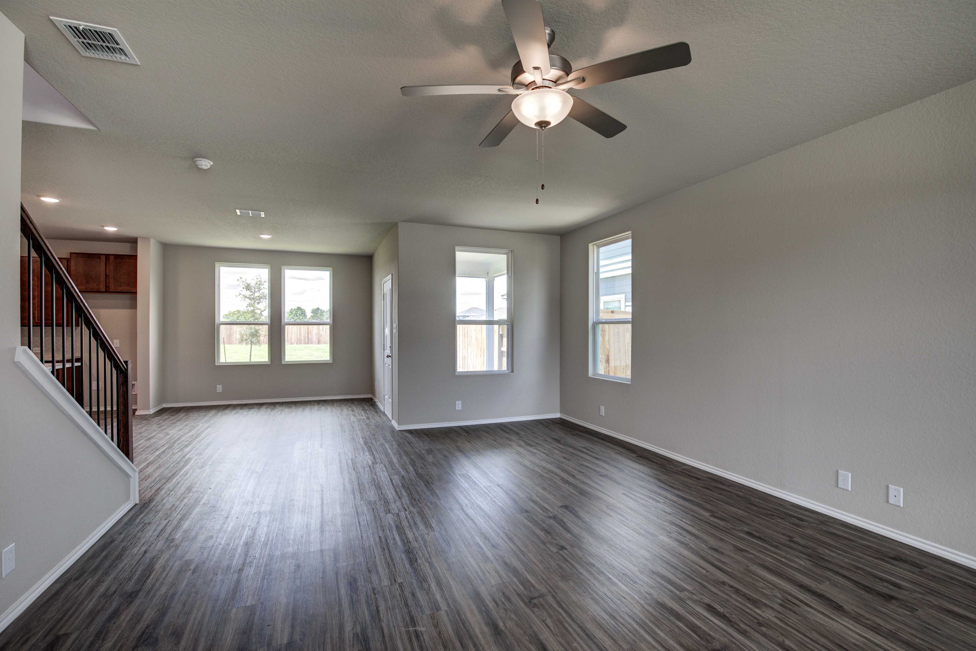 Spacious open-concept living room in The Murray home design with hardwood floors, ceiling fan, and large windows