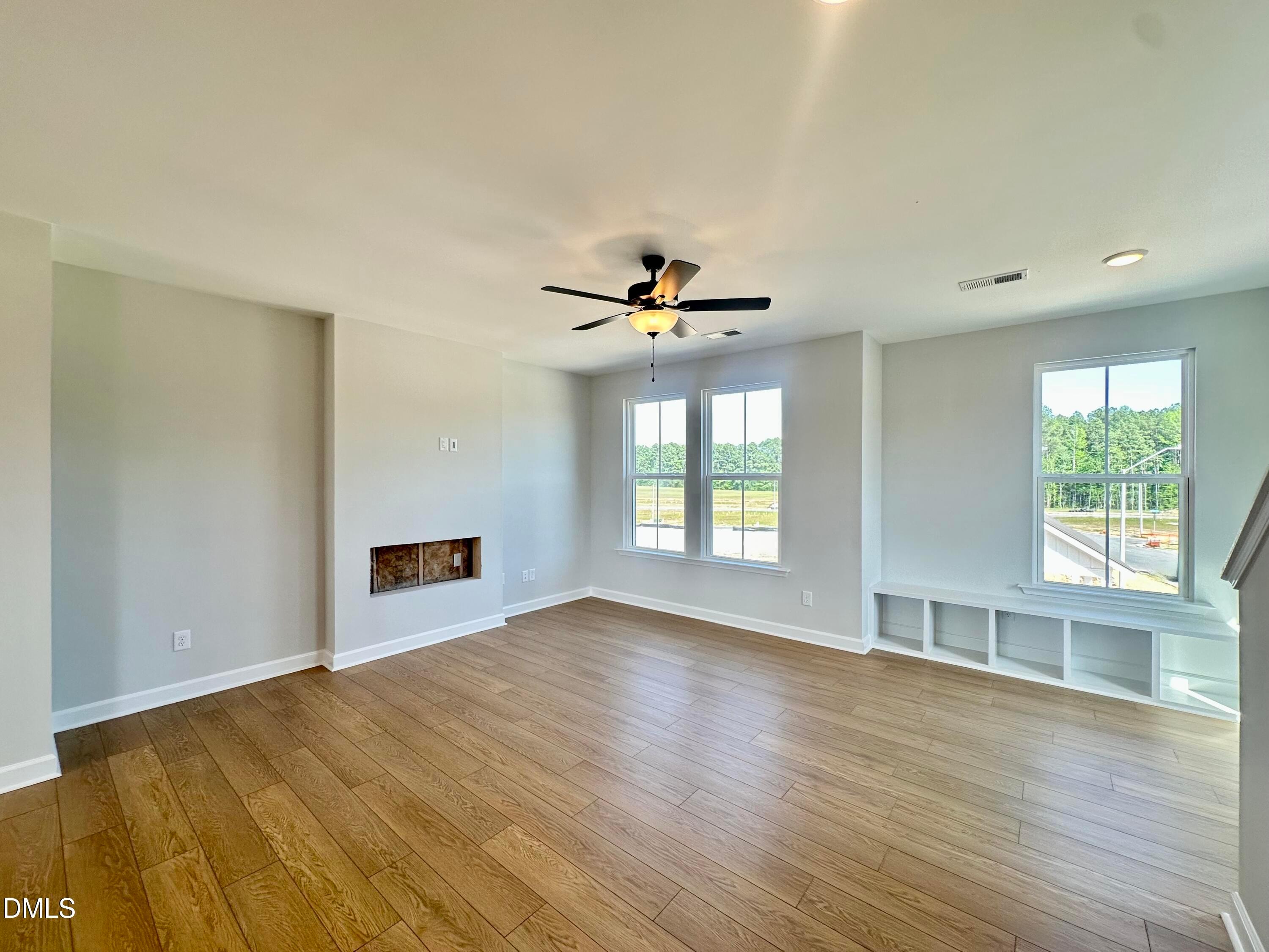 Spacious living room with hardwood floors, ceiling fan, large windows overlooking woods, fireplace, built-in shelves in Davidson Homes The Avery, Knightdale, NC