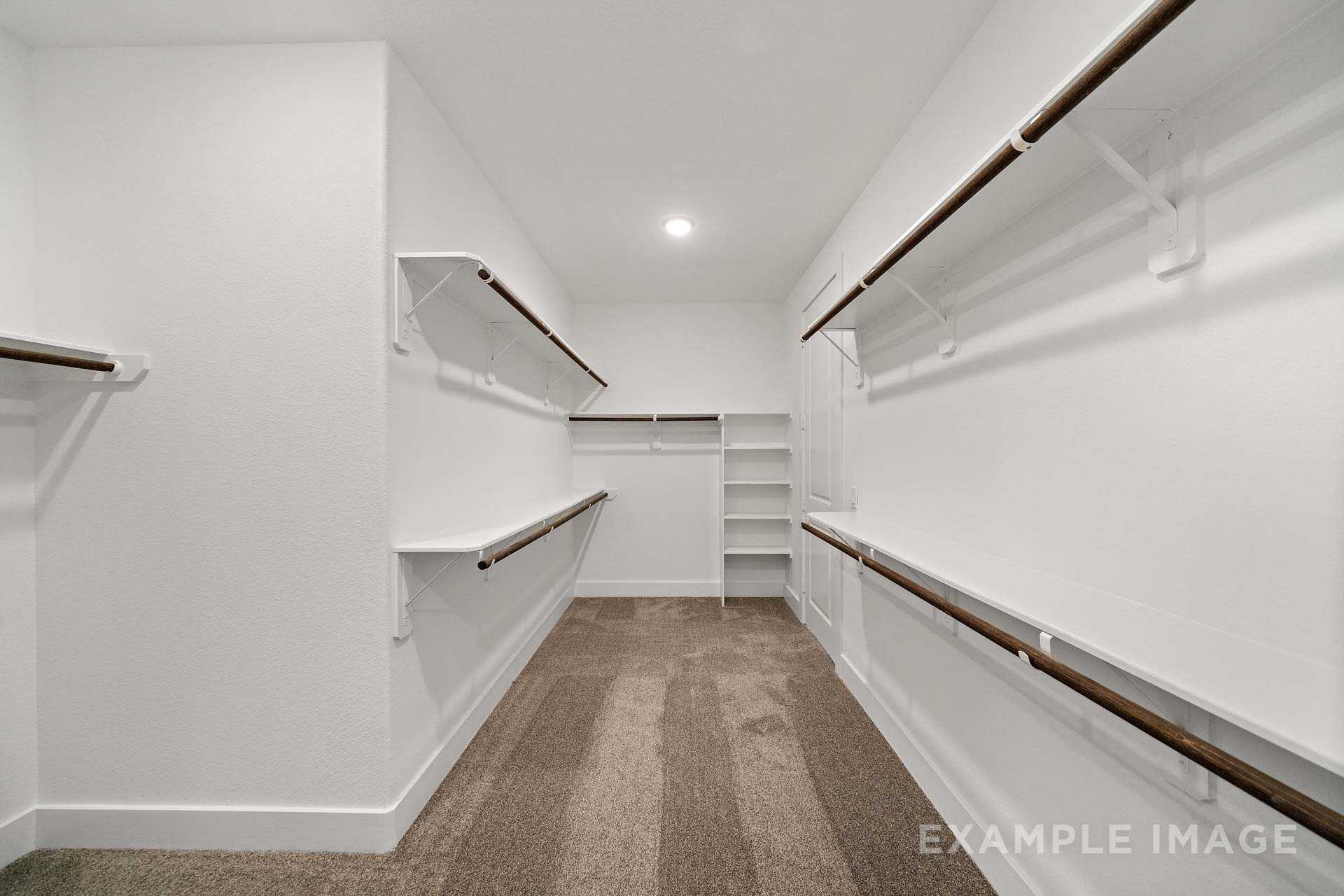 Spacious walk-in master closet in The Victoria A with wooden shelves, hanging rods, white walls, and carpeted floor