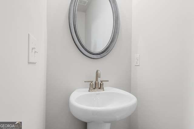 Elegant powder room featuring white pedestal sink, chrome faucet, and oval mirror in Davidson Homes The Glenwood C at Wehunt Meadows, Hoschton, GA