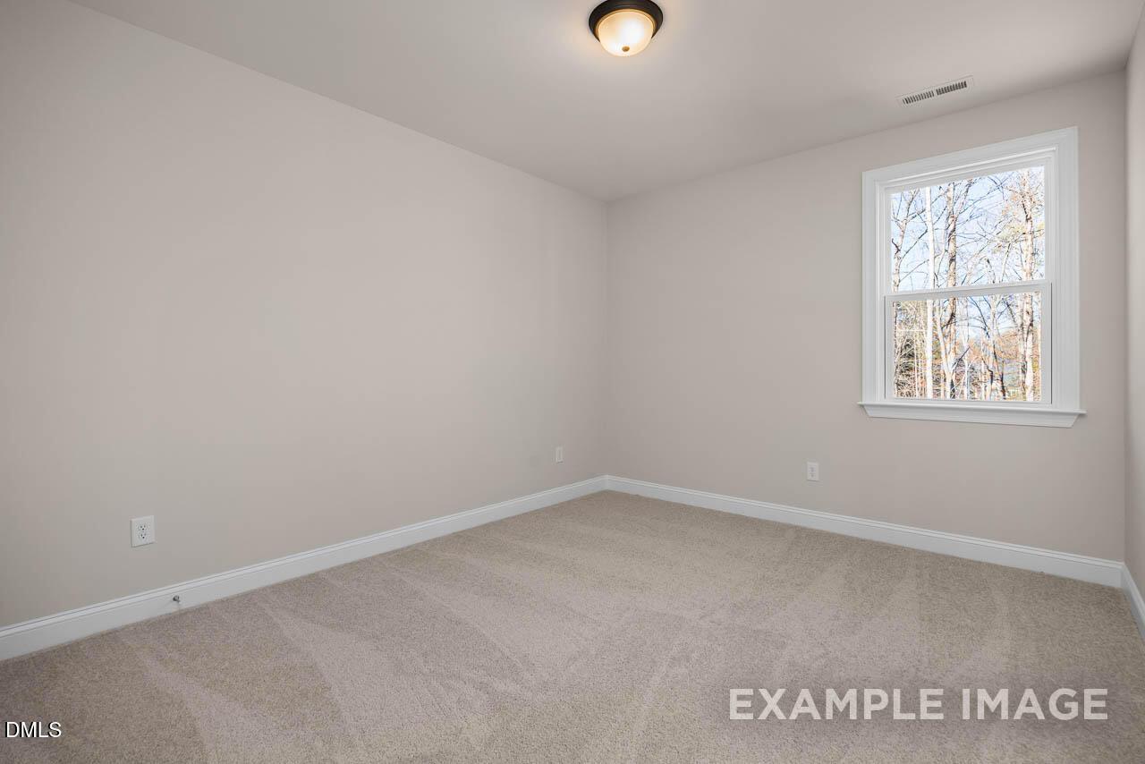Spacious empty bedroom with neutral beige walls, plush carpet, and window overlooking trees in The Crawford D, Angier, NC