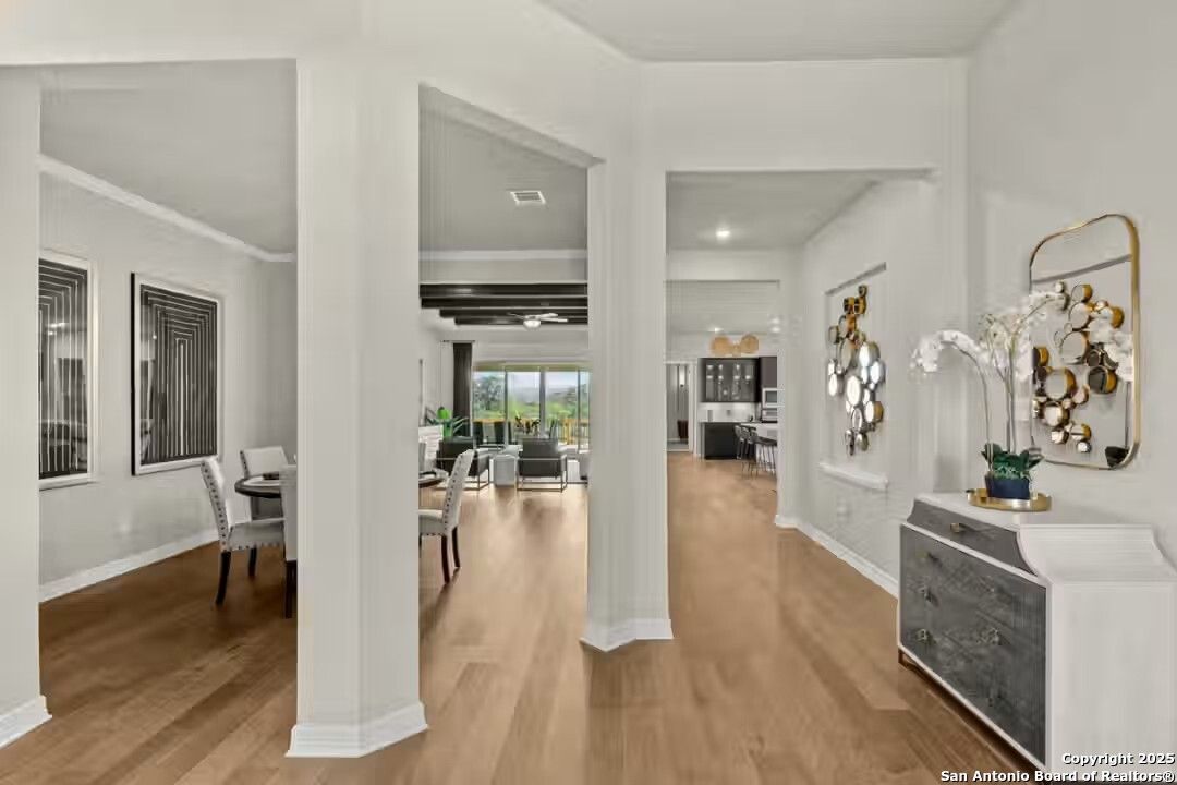 Elegant open dining area with hardwood floors, white columns, and backyard view through large windows in The Summerlin B home, Castroville, Texas