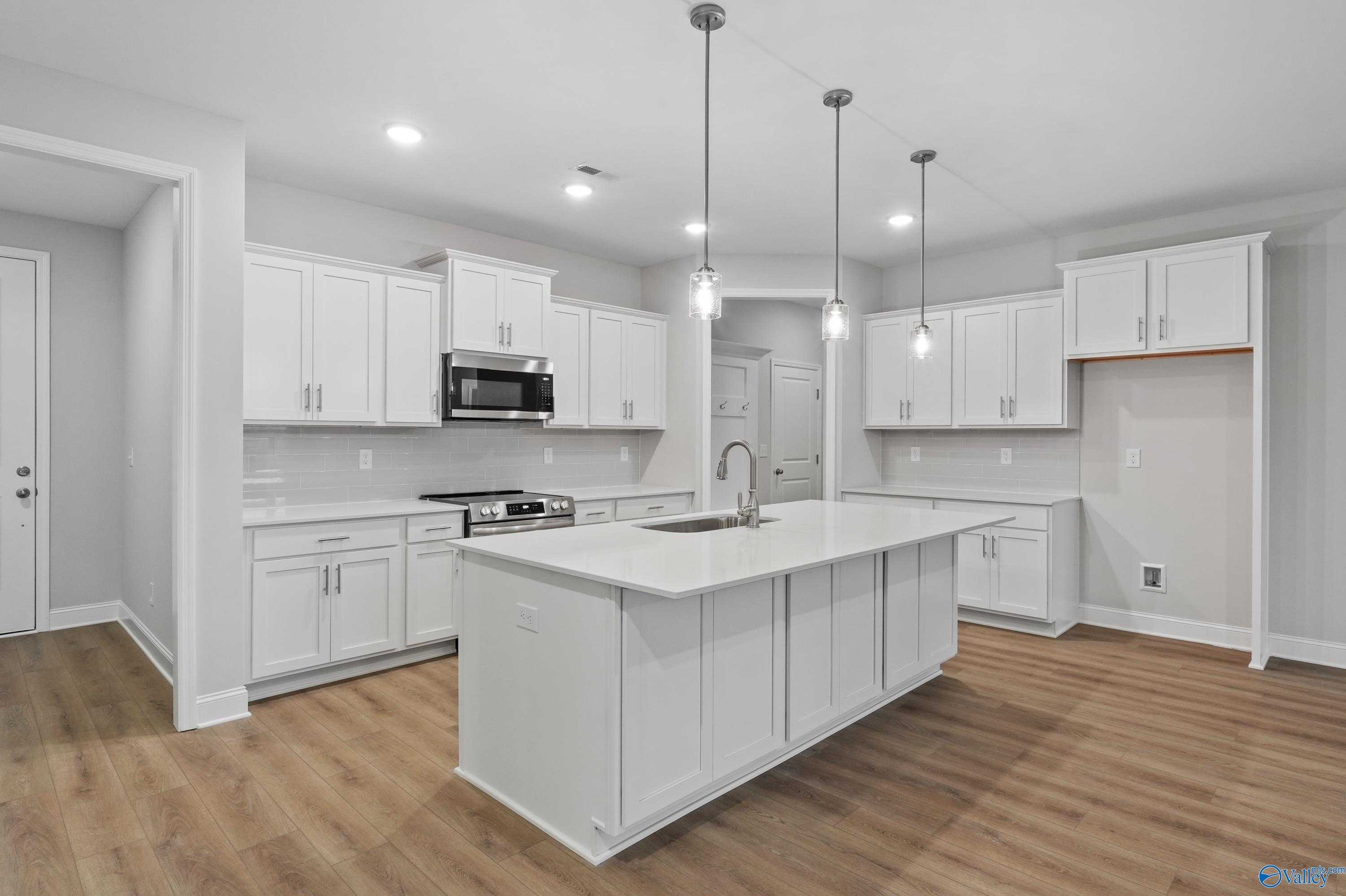 Modern white kitchen with quartz island, stainless appliances, and pendant lights in Davidson Homes The Lanier, Harvest, Alabama