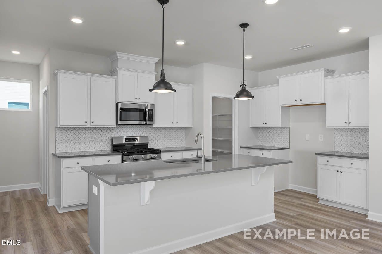 Modern white kitchen with shaker cabinets, subway tile backsplash, granite island, and stainless appliances in The Adalynn A, Lillington NC