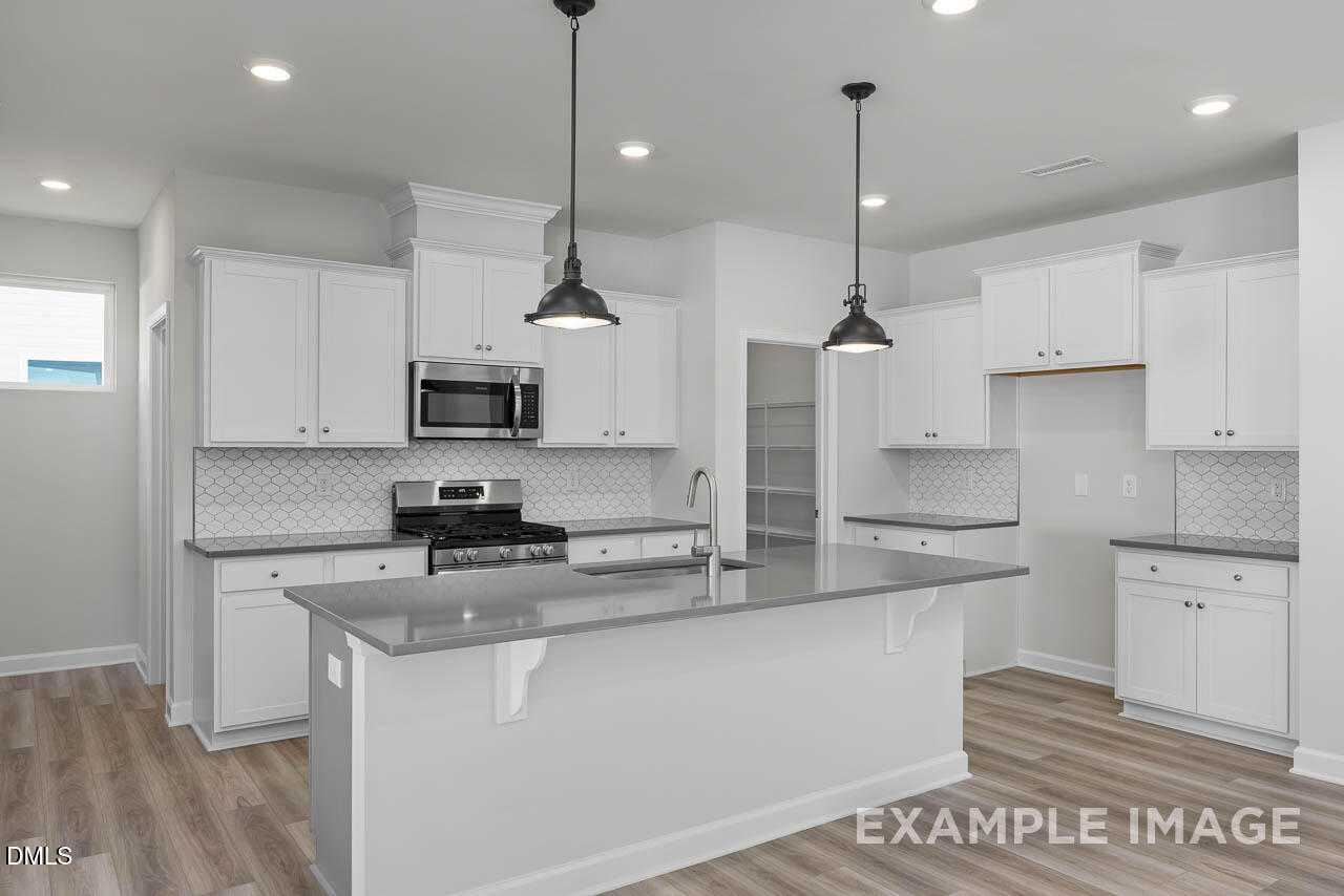 Modern white kitchen with shaker cabinets, subway tile backsplash, granite island, and stainless appliances in The Adalynn A, Lillington NC